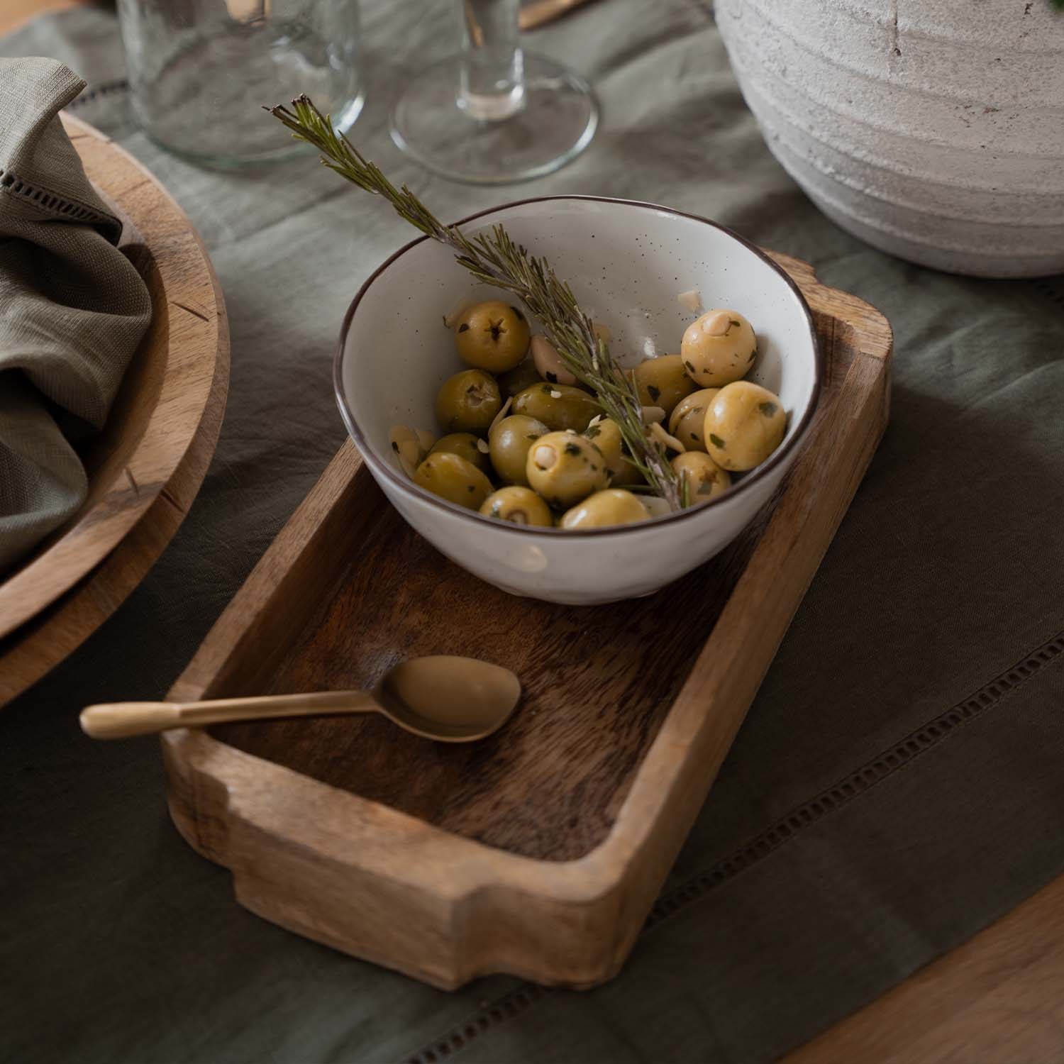 Ciotola in ceramica bianca con olive verdi e rametto di rosmarino su vassoio in legno