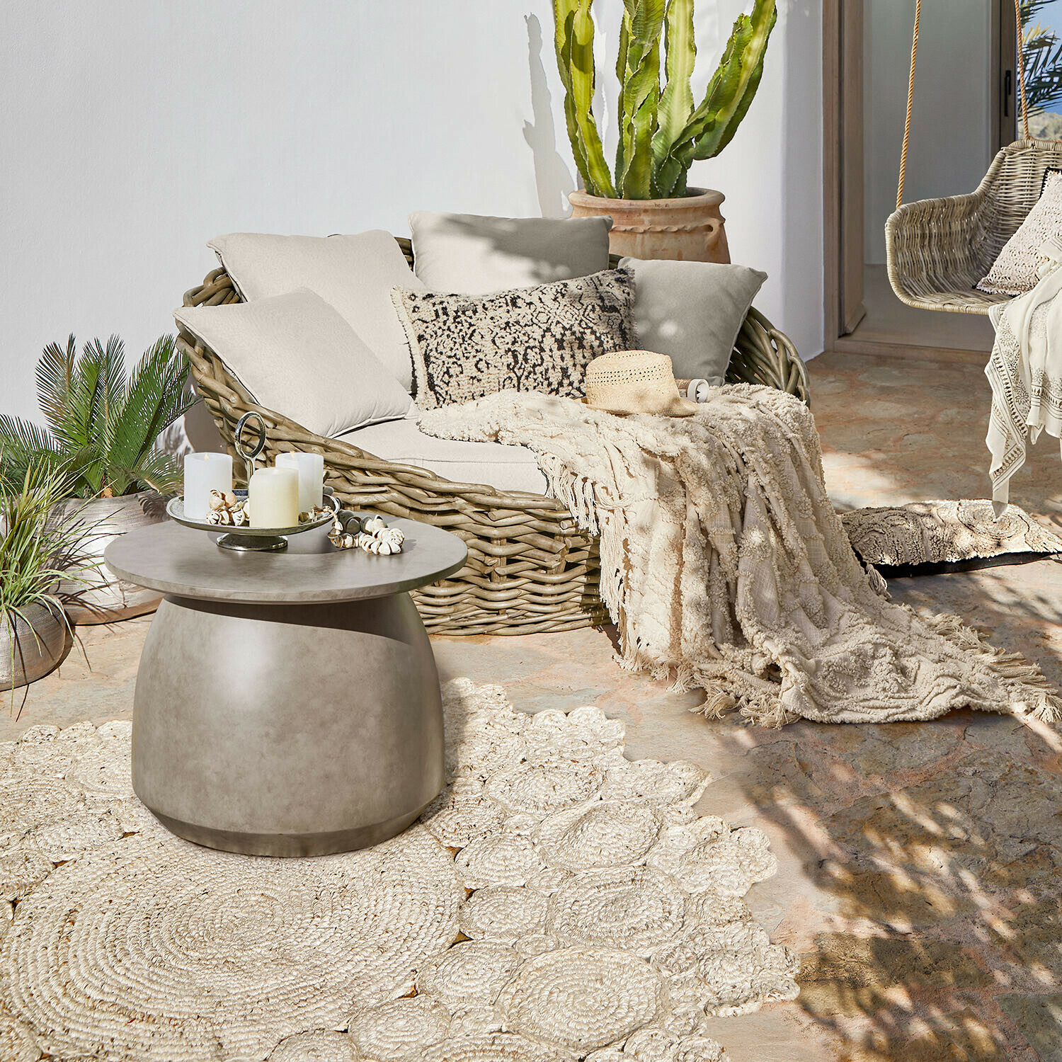 Divano ovale in rattan con cuscini crema e coperta su terrazza con tavolino in cemento