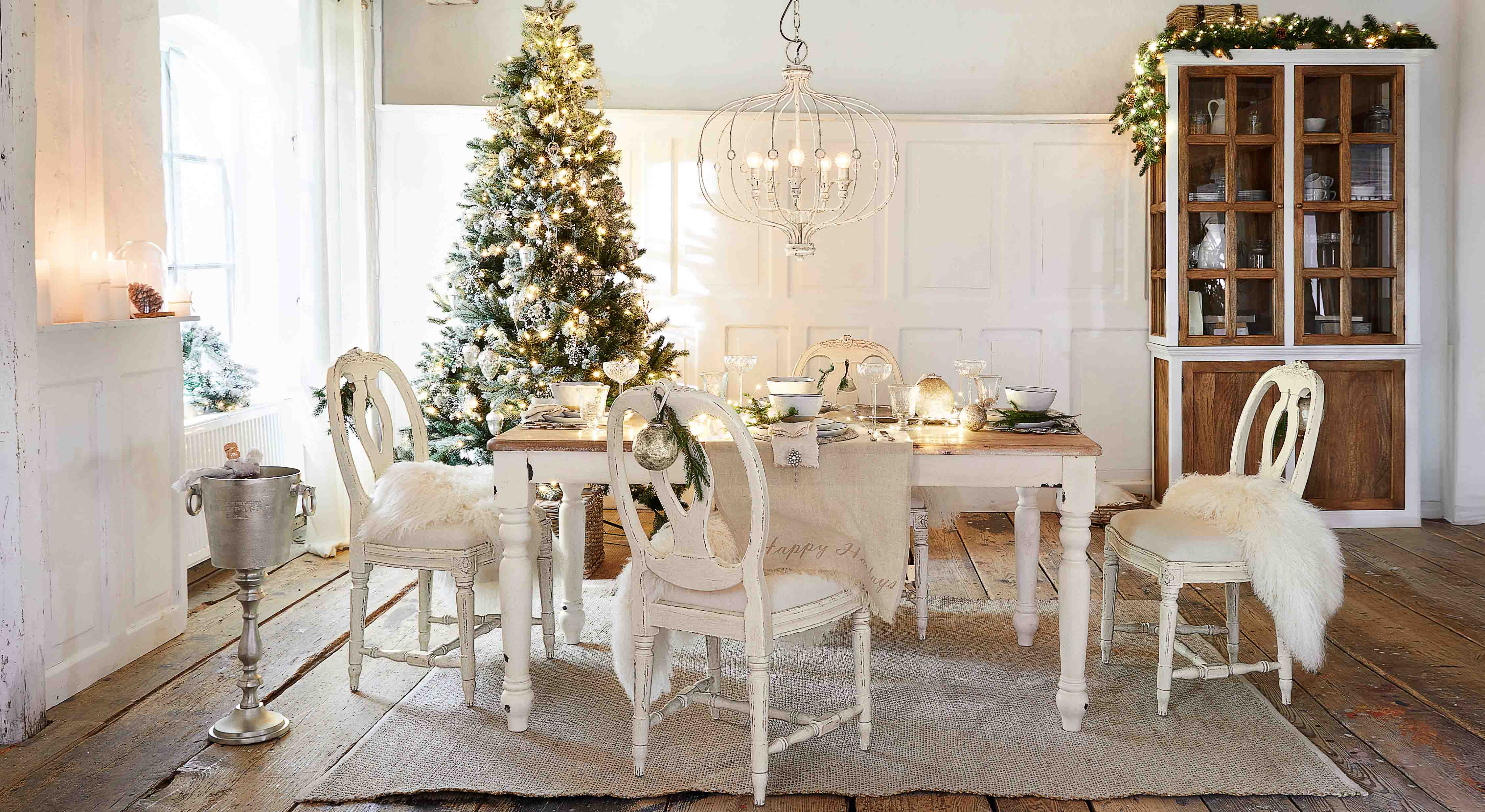 Sala da pranzo con tavolo e sedie in legno bianco decorate per Natale con albero e luci