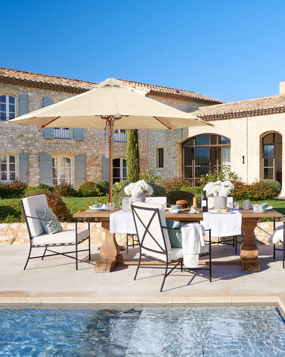 Set di mobili da giardino con tavolo in legno e ombrellone beige vicino alla piscina in stile rustico