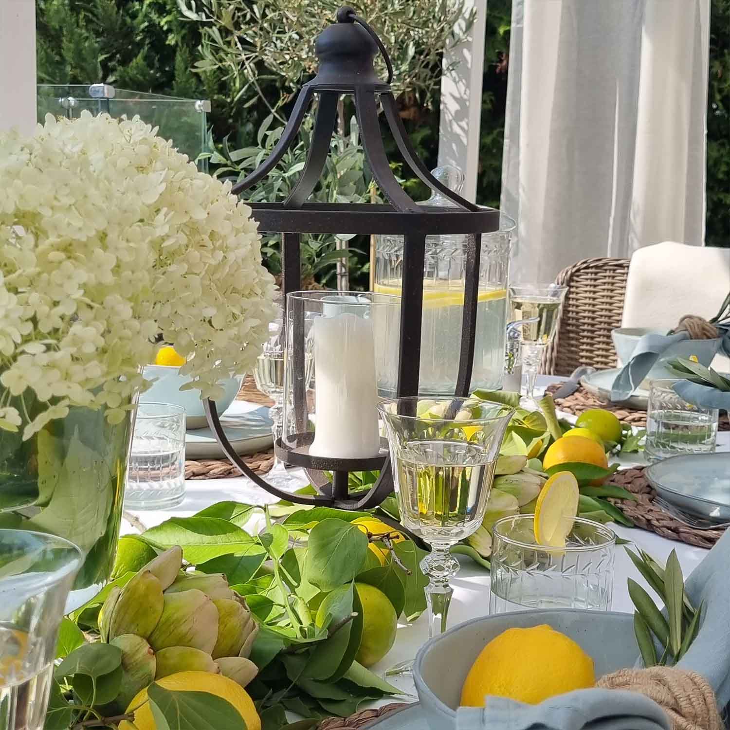 Lanterna in metallo nero con candela bianca su tavolo estivo decorato con limoni e foglie verdi