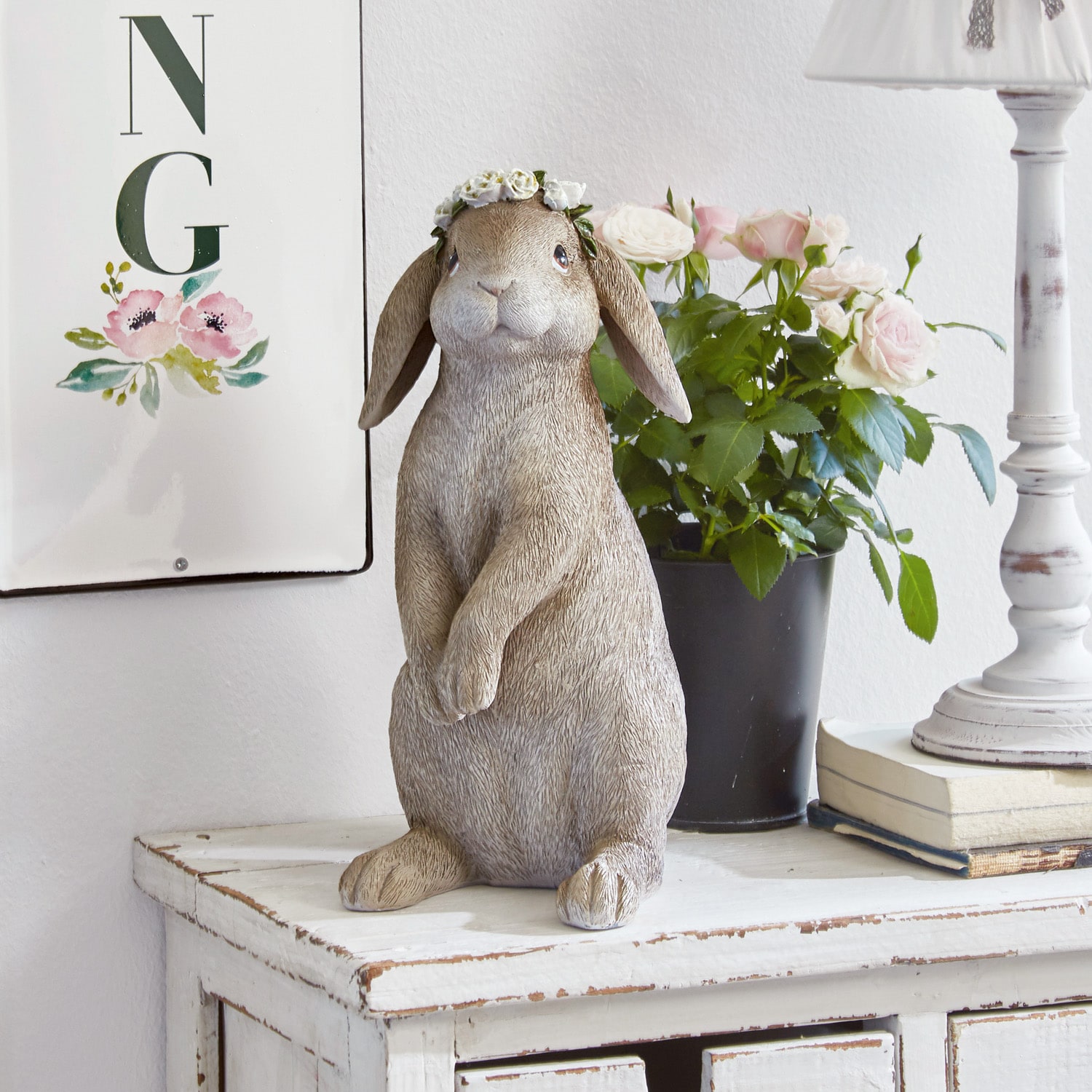 Statua decorativa di coniglio beige con corona di fiori su comò bianco in legno