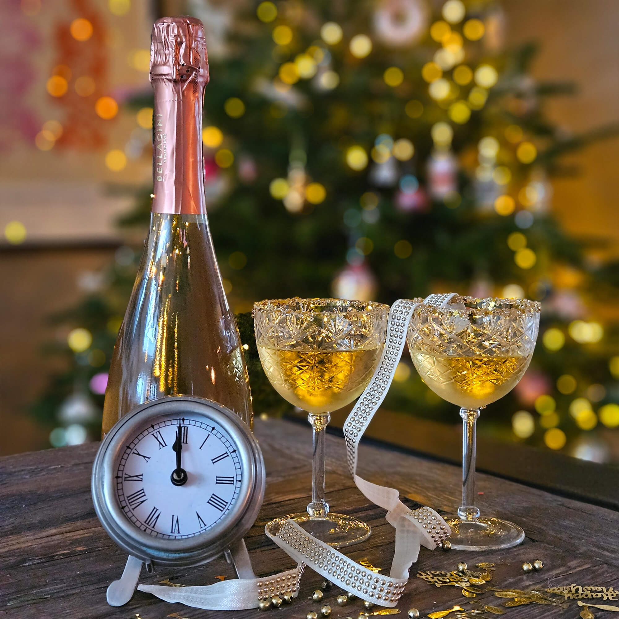 Bottiglia di champagne con foglio rosa, due bicchieri di cristallo con bevanda dorata e orologio su tavolo in legno
