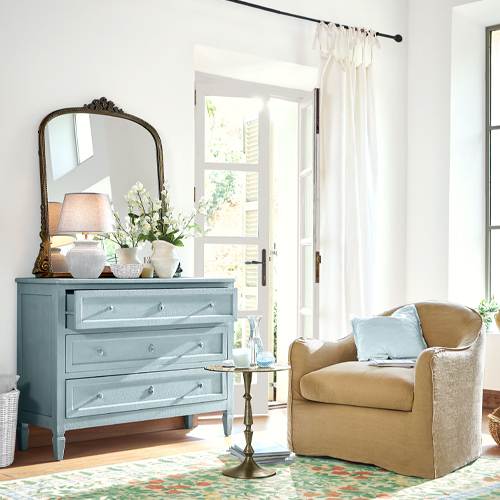 Comò in legno azzurro chiaro con specchio e decorazioni in soggiorno luminoso con poltrona beige