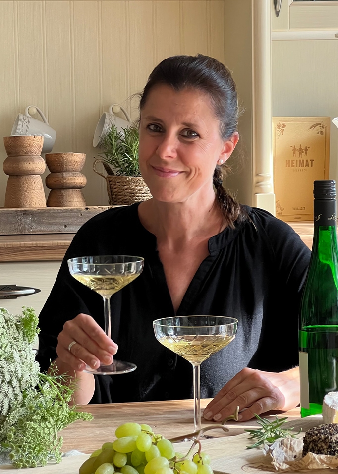 Donna con camicia nera che tiene un bicchiere di vino bianco a tavola con uva e formaggi