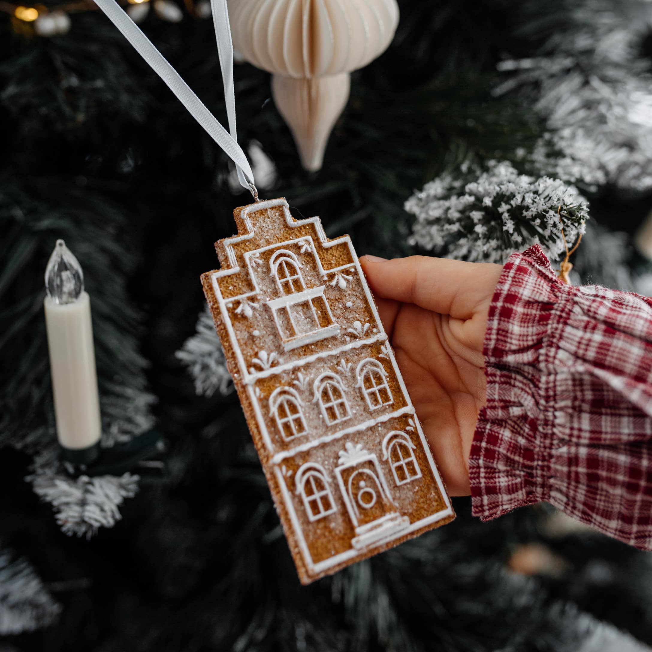 Decorazione natalizia a forma di casetta di pan di zenzero con motivo bianco, appesa a un nastro bianco