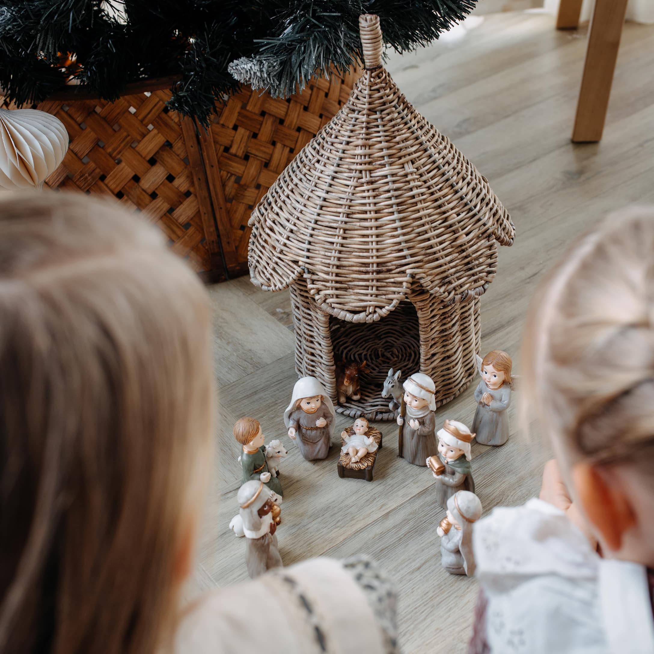 Bambini guardano presepe natalizio con figure in ceramica e casetta in vimini sul pavimento