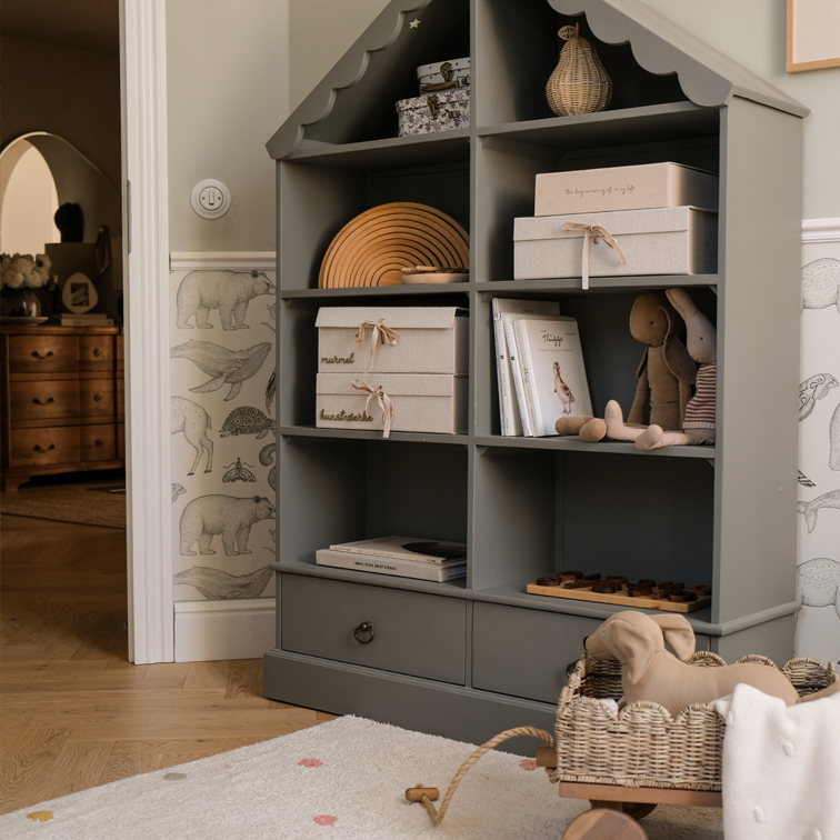 Scaffale grigio in legno a forma di casa con scatole, libri e peluche in camera dei bambini