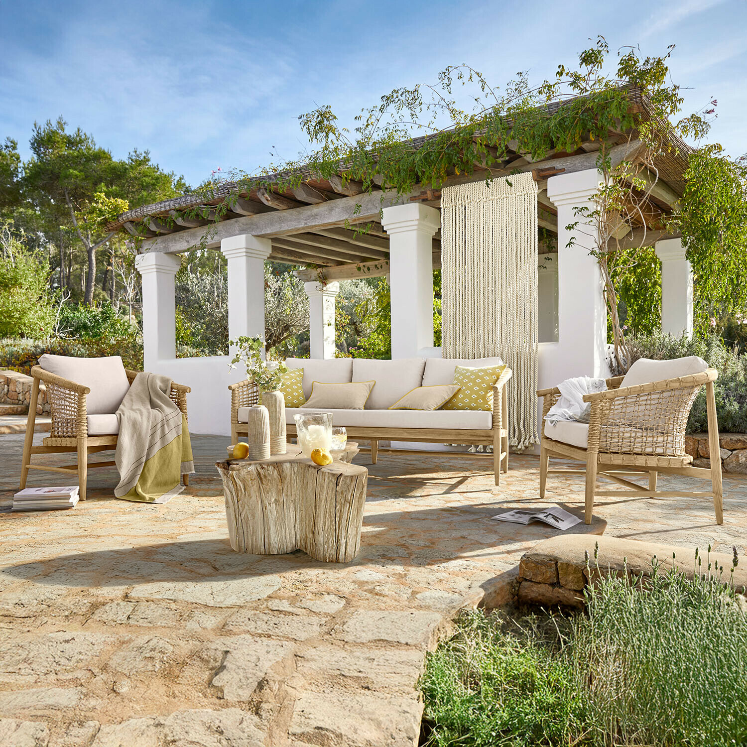 Set divano e poltrone Roselva Set di mobili da giardino in legno chiaro con cuscini beige su patio in pietra e tavolo naturale rustico