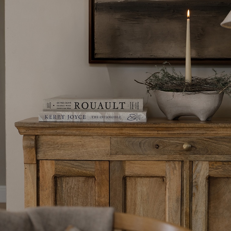 Credenza in legno con due libri e candela accesa in ciotola di ceramica su tavolo decorativo