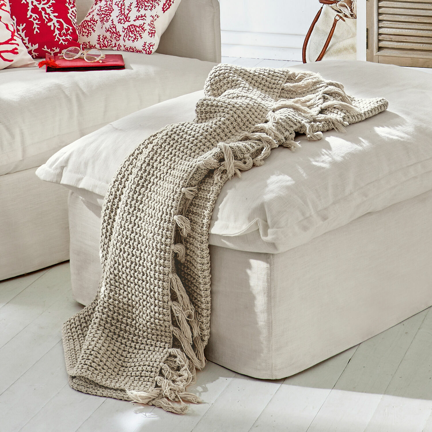 Plaid Kendall Coperta beige lavorata a maglia con frange su pouf chiaro in soggiorno moderno