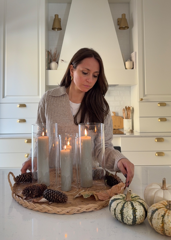 Composizione autunnale con candele grigie in cilindri di vetro e pigne naturali su vassoio intrecciato
