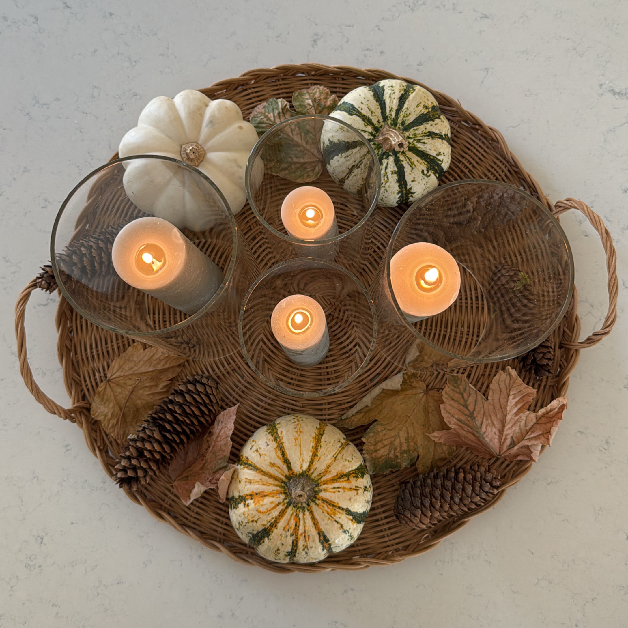 Composizione autunnale decorativa con zucche, pigne e candele su vassoio in vimini per tavolo