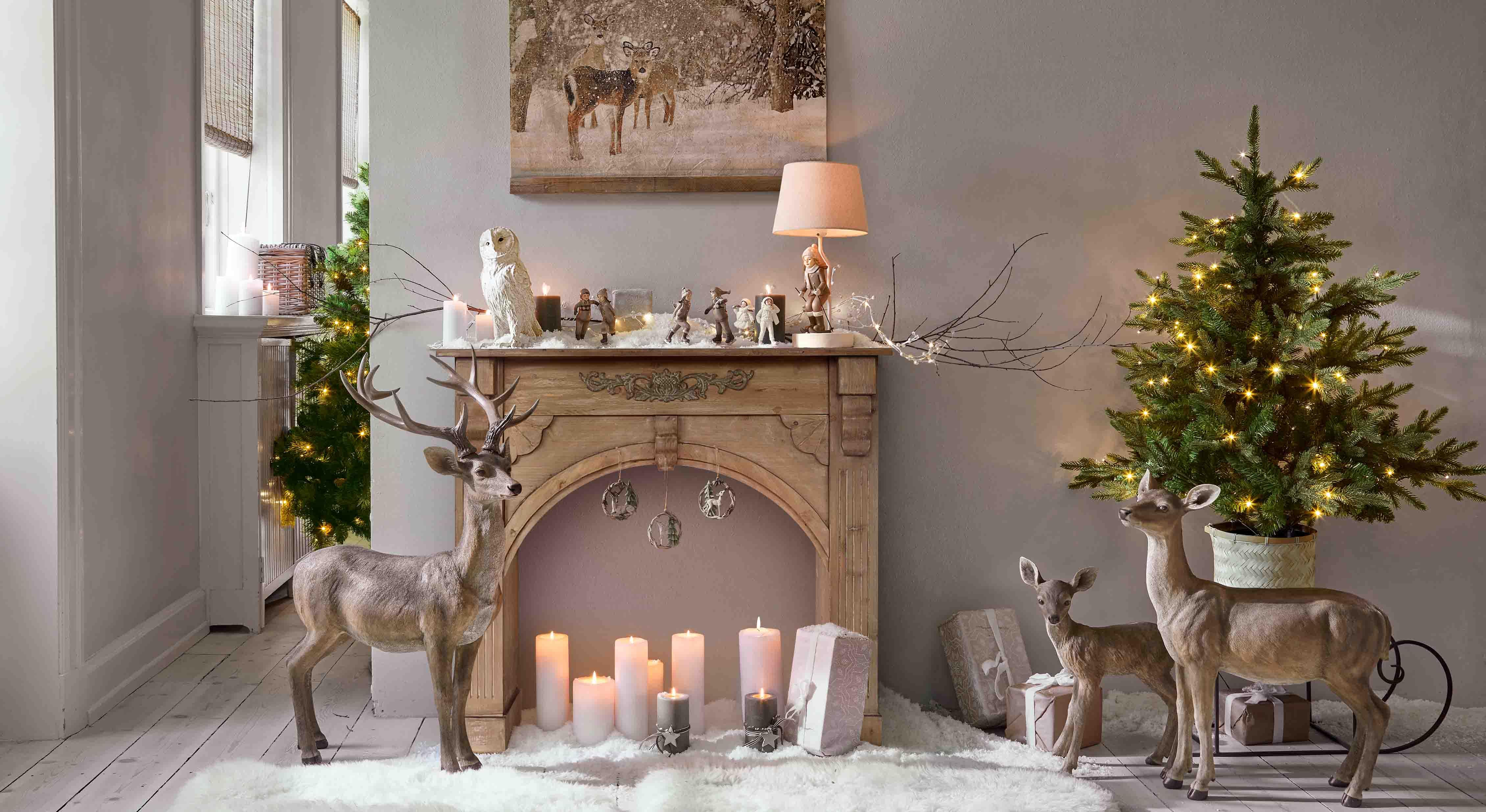 Decorazione natalizia con figure di cervi marroni, candele e albero di Natale verde con luci LED