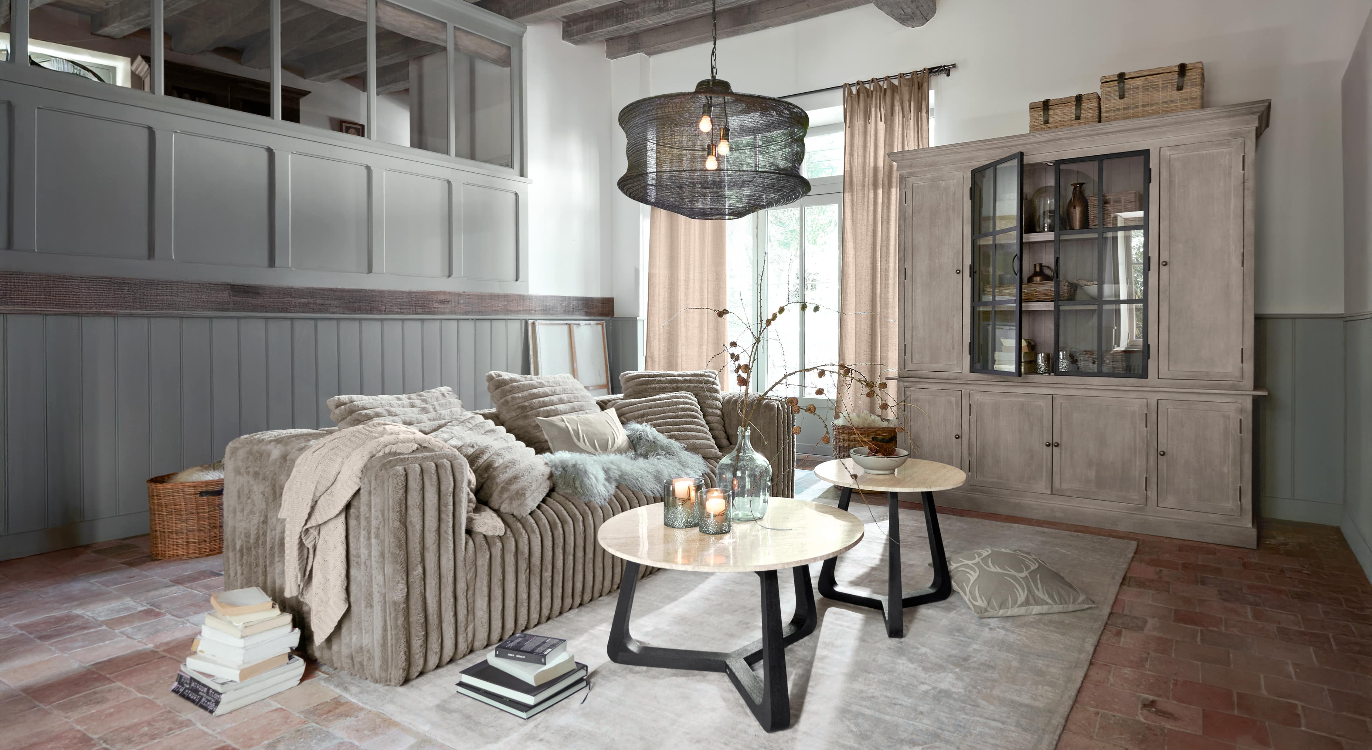 Soggiorno accogliente con divano beige in materiale morbido e due tavolini rotondi con piani in marmo