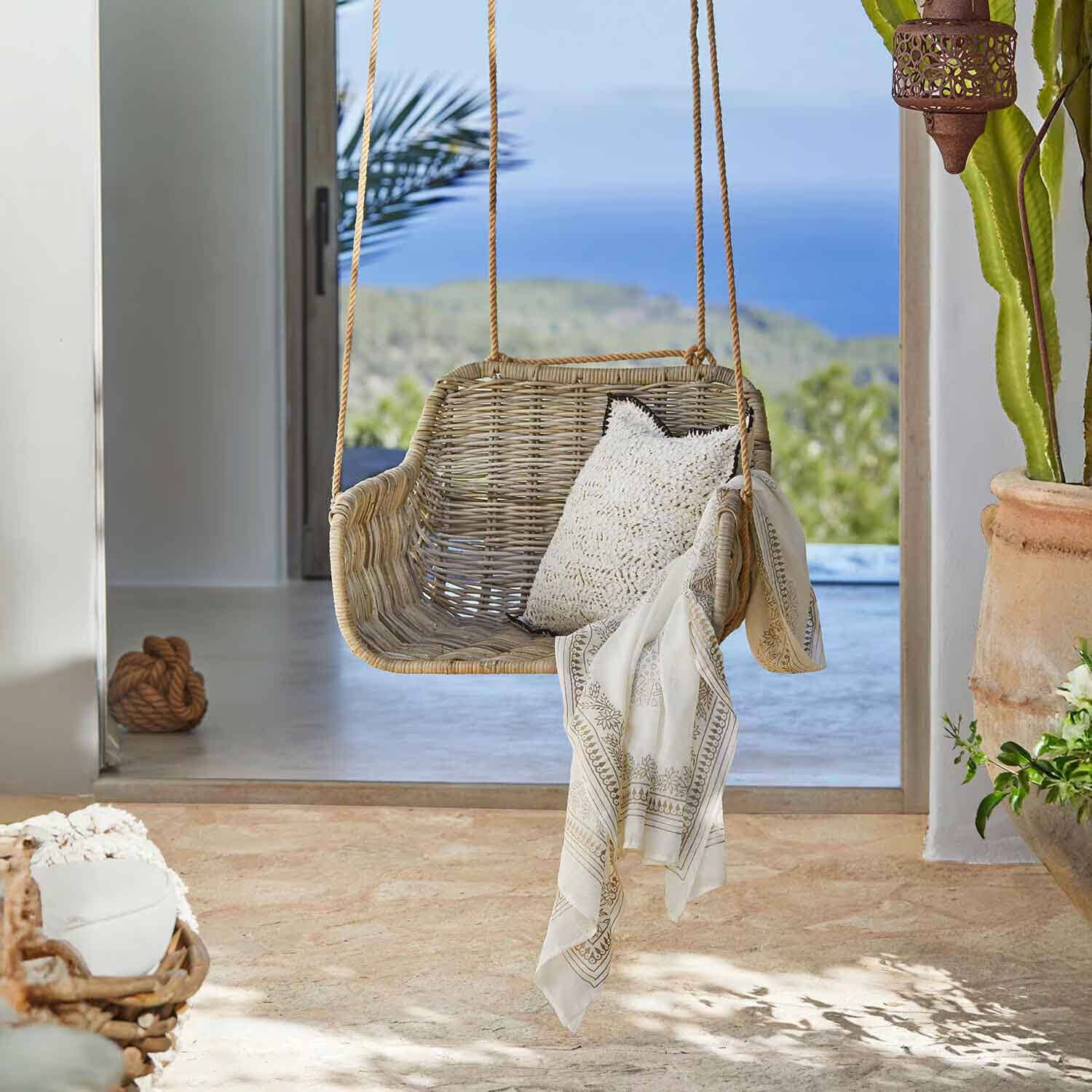 Altalena in rattan colore naturale con cuscino bianco e sciarpa decorativa in interno luminoso