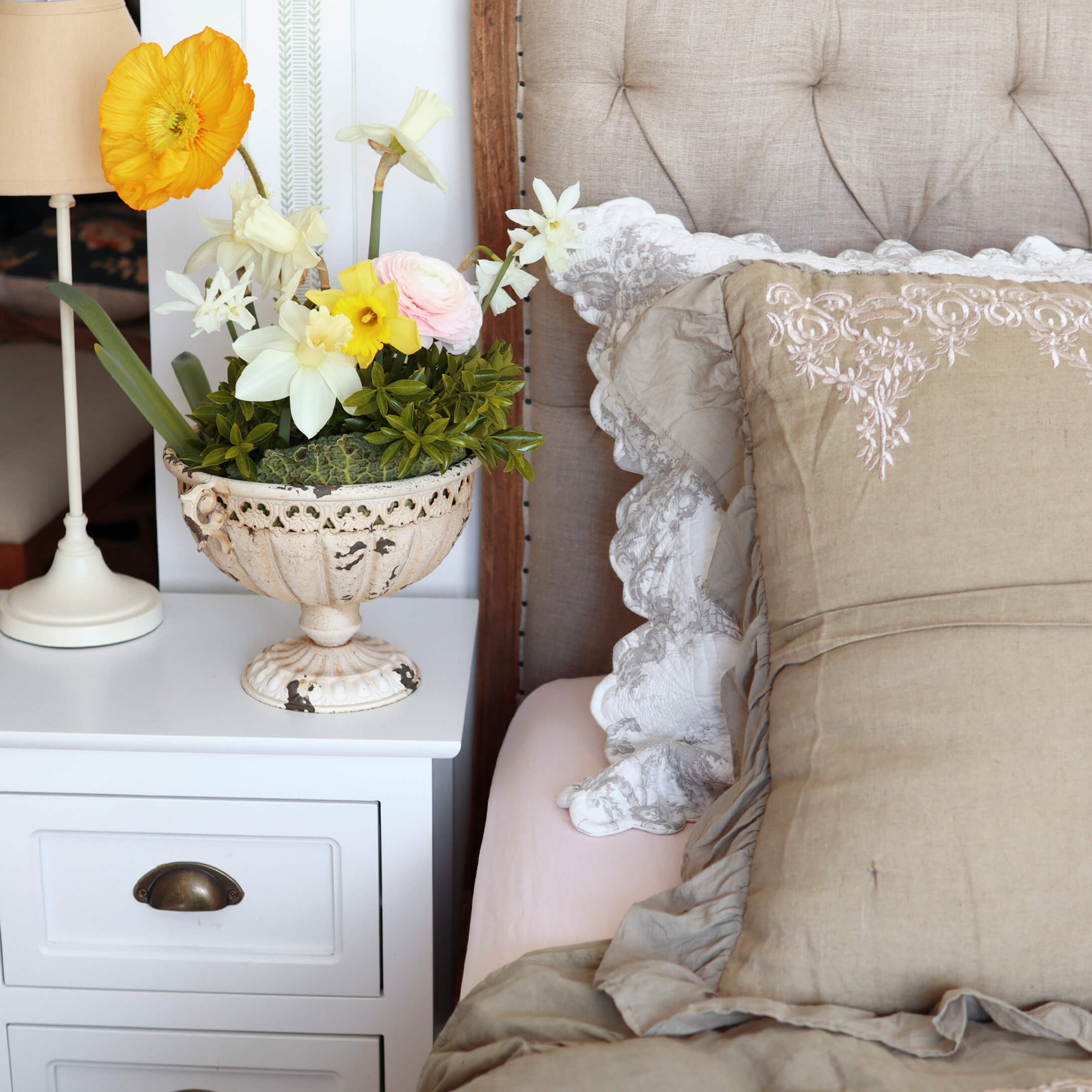 Vaso decorativo bianco in ceramica con fiori colorati su comodino bianco accanto al letto