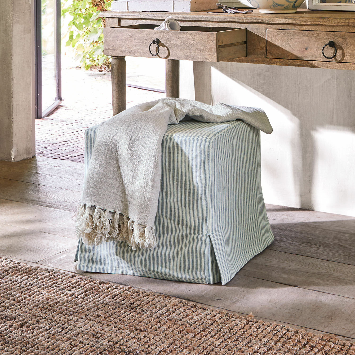 Pouf Ulysette Pouf quadrato in cotone a righe blu e bianche con coperta crema su pavimento in legno
