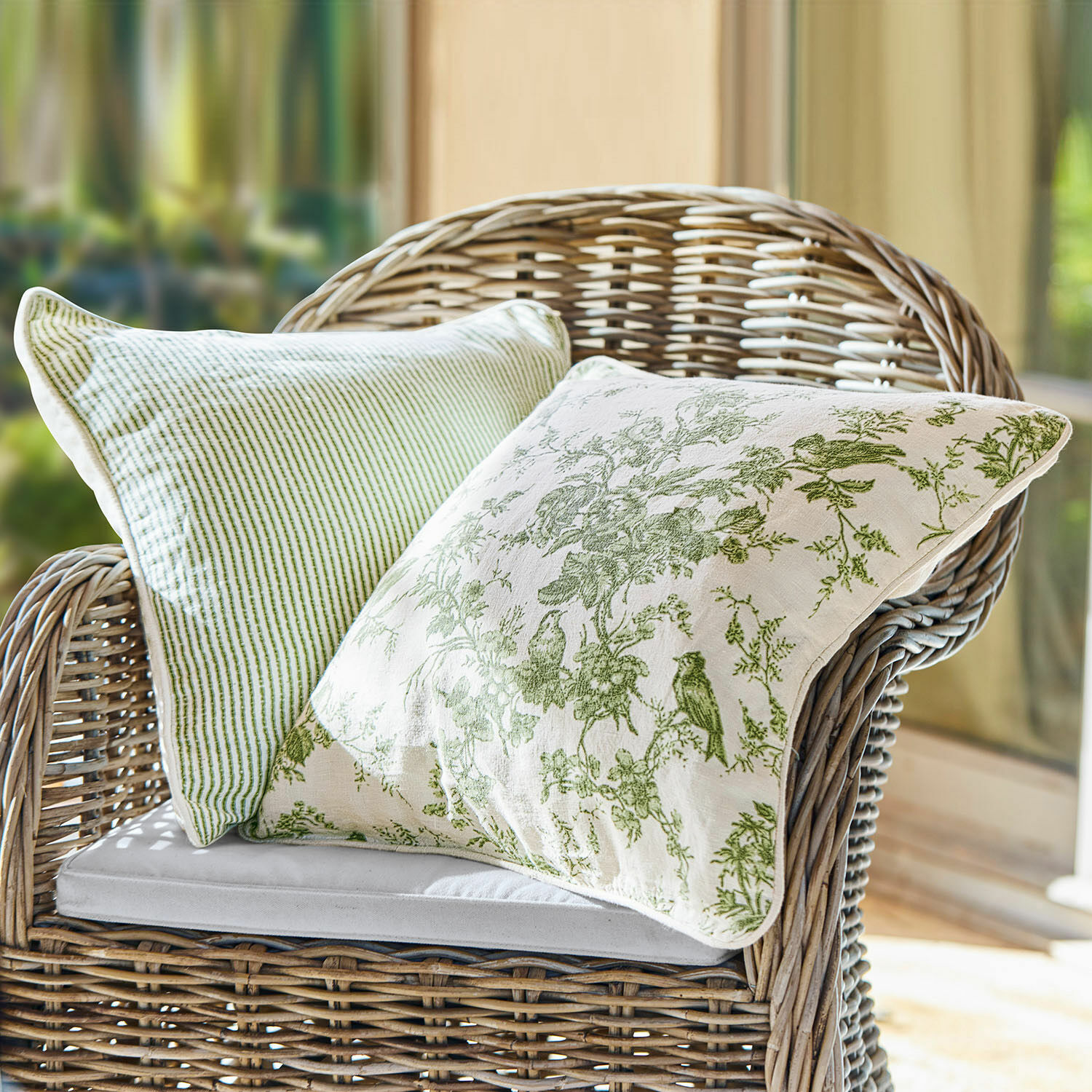 Coppia di copricuscini Mercier Due cuscini decorativi verdi in cotone su una poltrona in vimini in ambiente luminoso