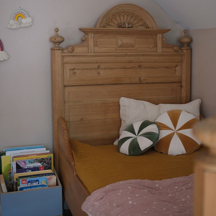 Letto in legno massiccio con testiera decorata, cuscini e libri in camera per bambini