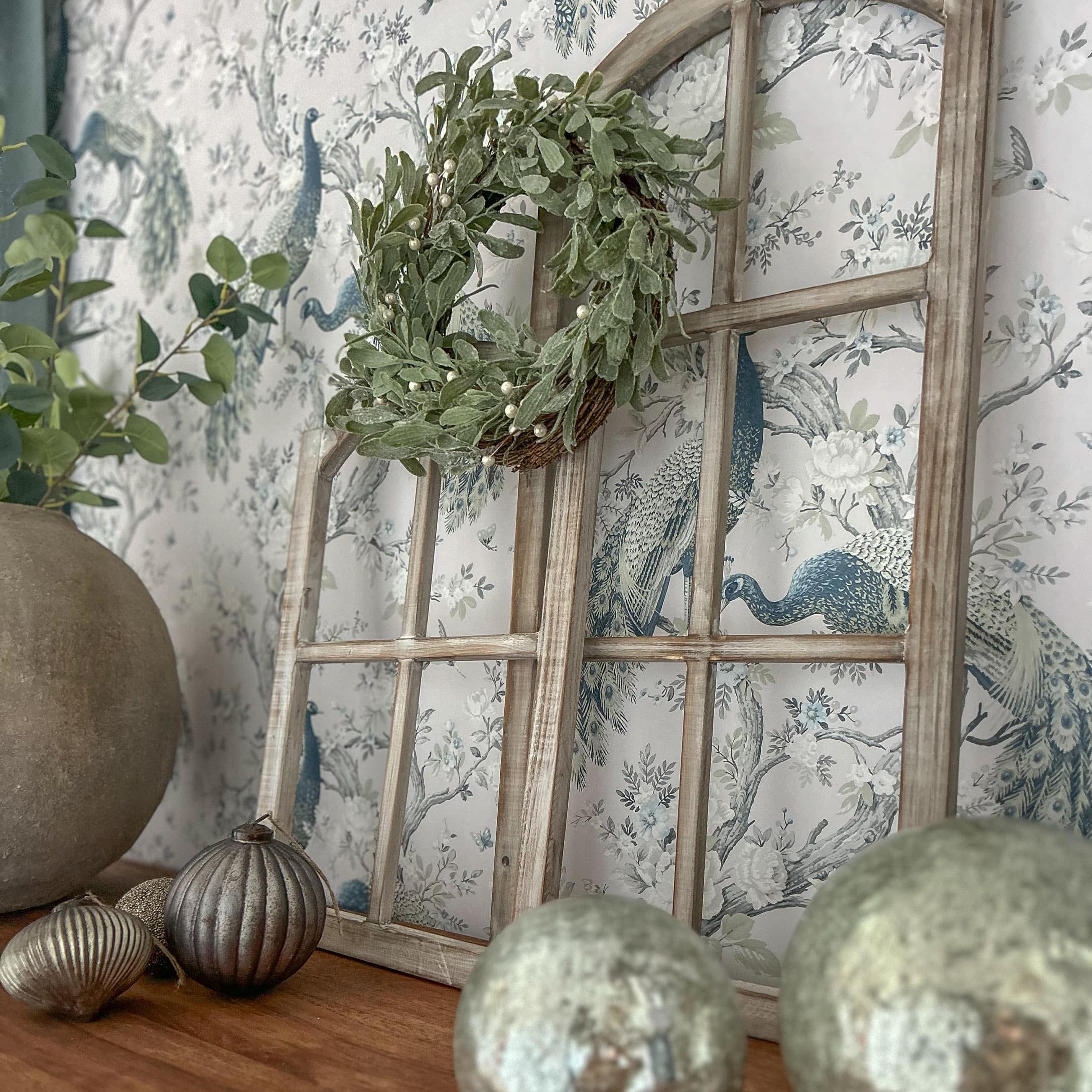 Cornice finestra in legno decorativa con corona verde e ornamenti metallici su tavolo in legno
