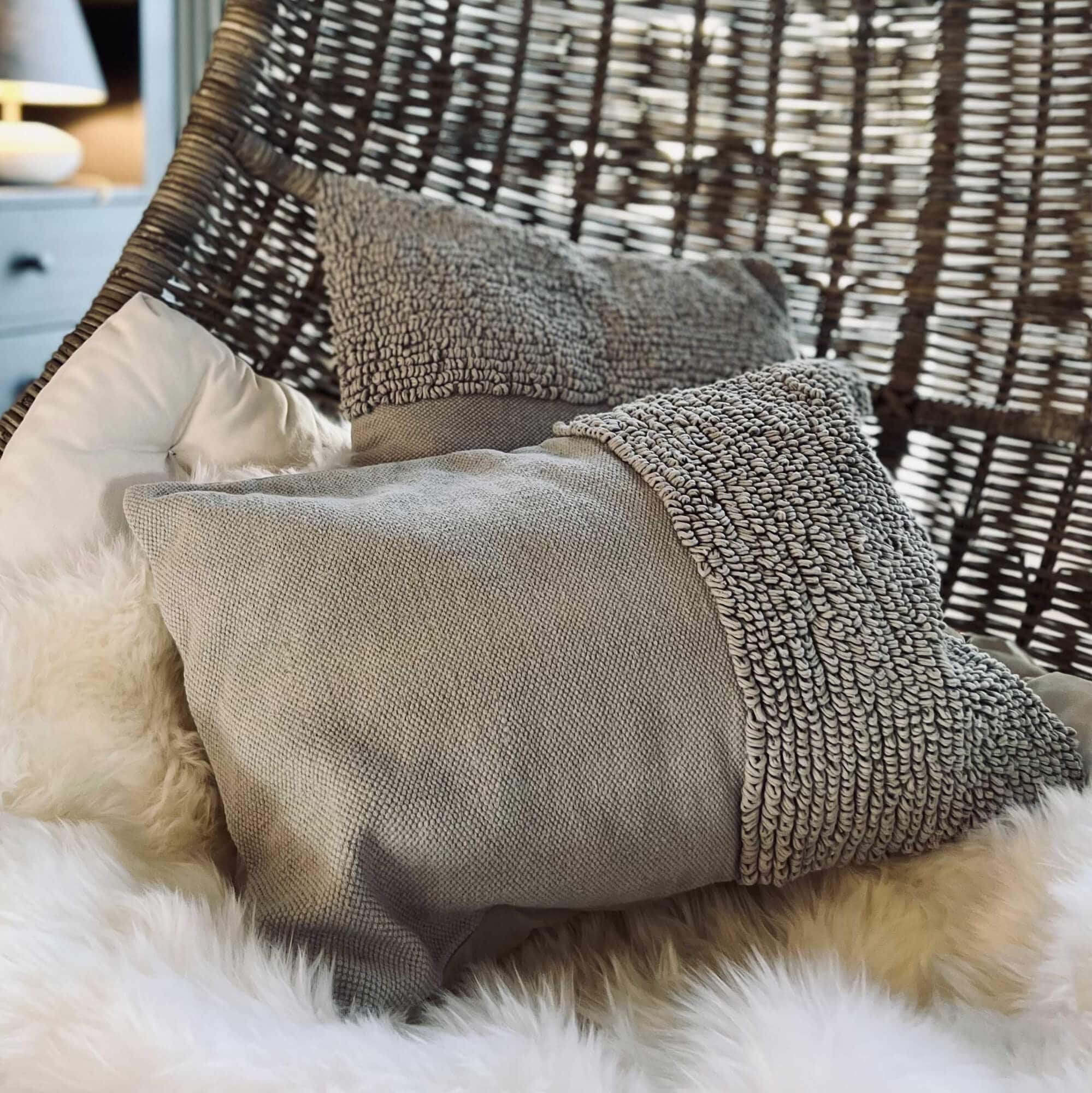 Cuscino grigio testurizzato su poltrona sospesa in vimini con coperta in pelliccia sintetica