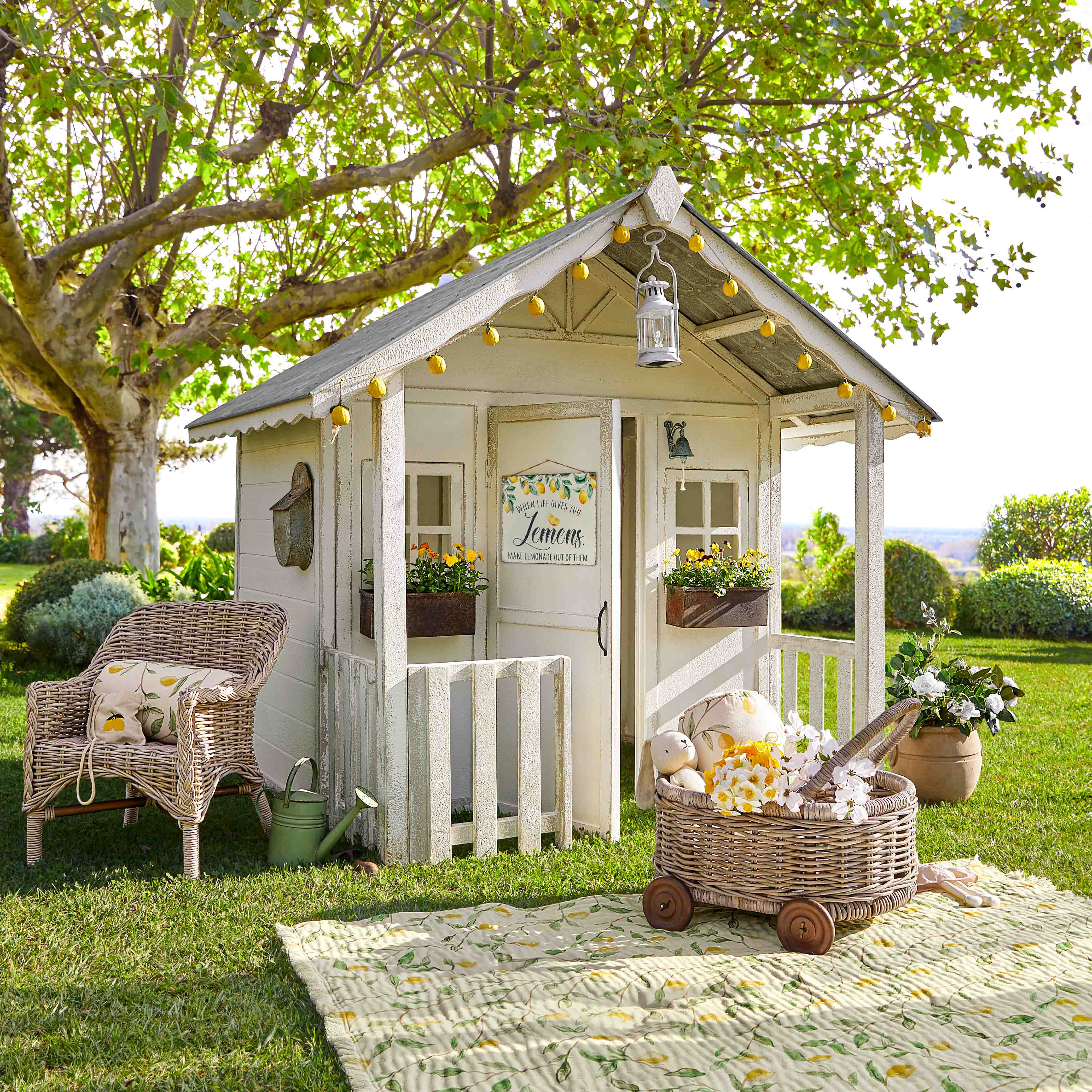 Casetta da giardino in legno bianco con luci decorative e fiori su prato verde