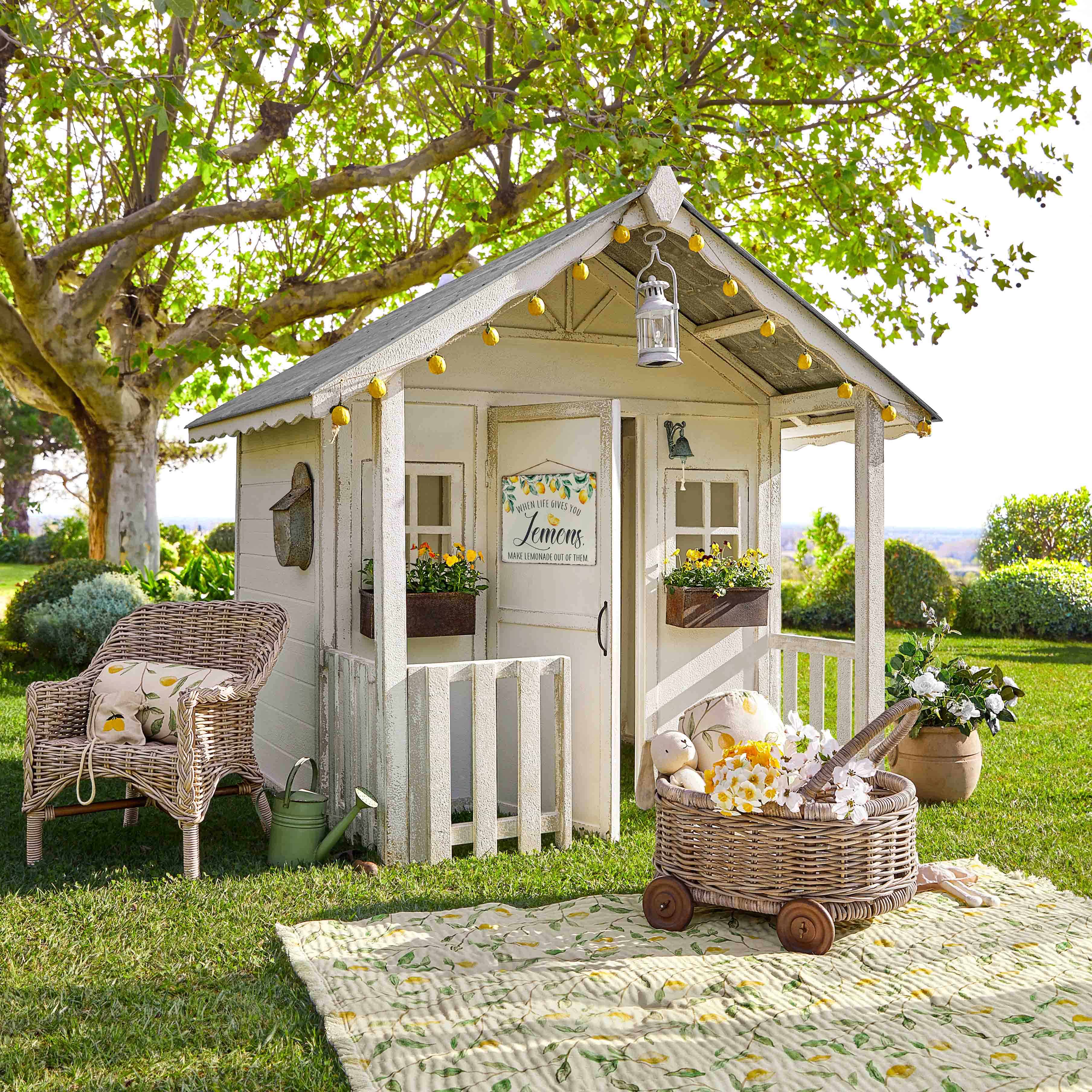 Casetta da giardino in legno bianco con luci decorative e fiori su prato verde