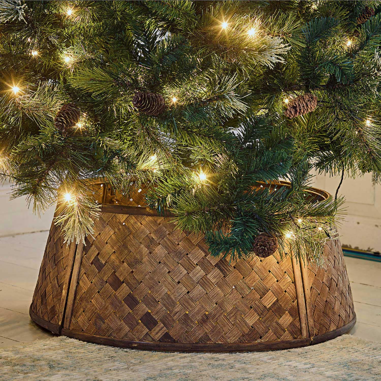 Cesto decorativo in legno intrecciato marrone sotto un albero di Natale con luci e pigne