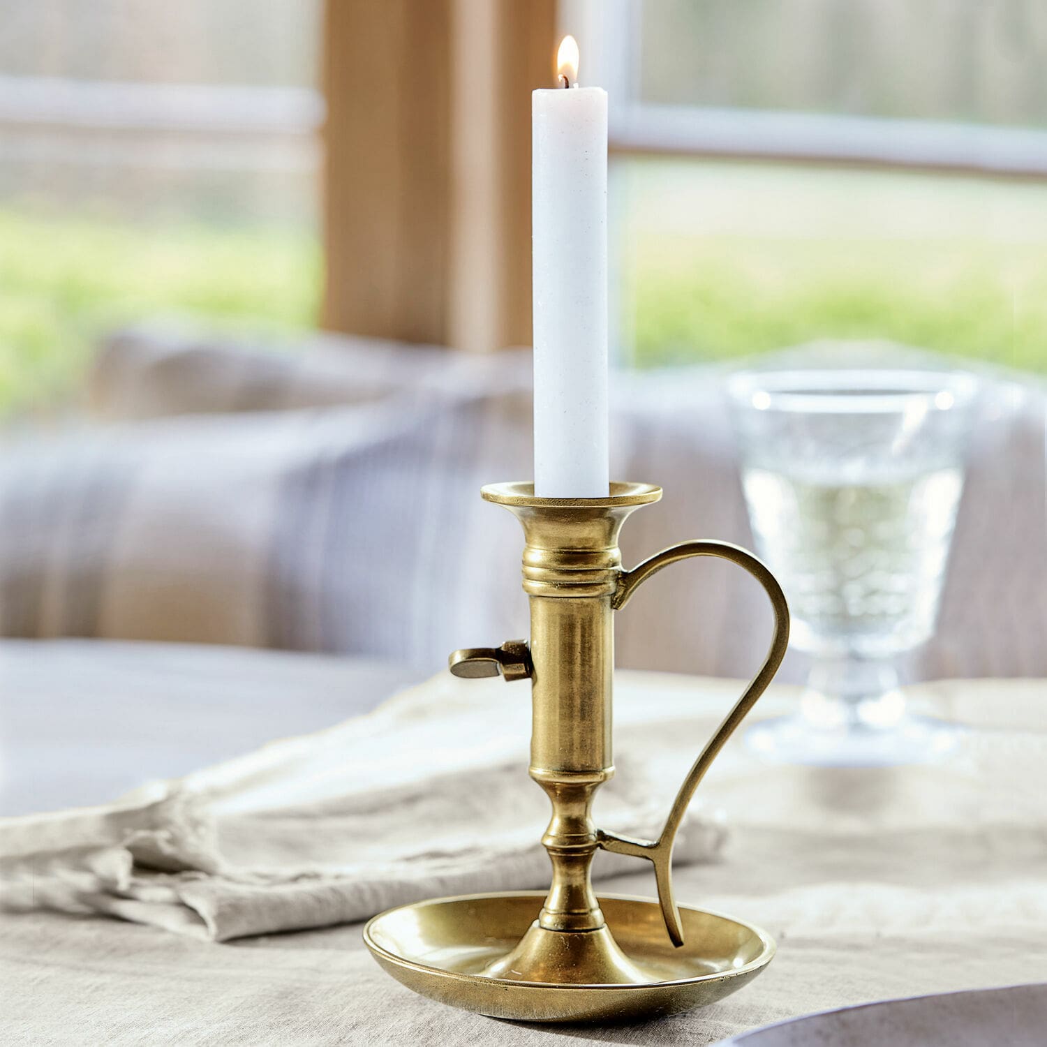 Candeliere Carmel Portacandela in ottone con manico e candela bianca su tovaglia di lino, decorazione tavola