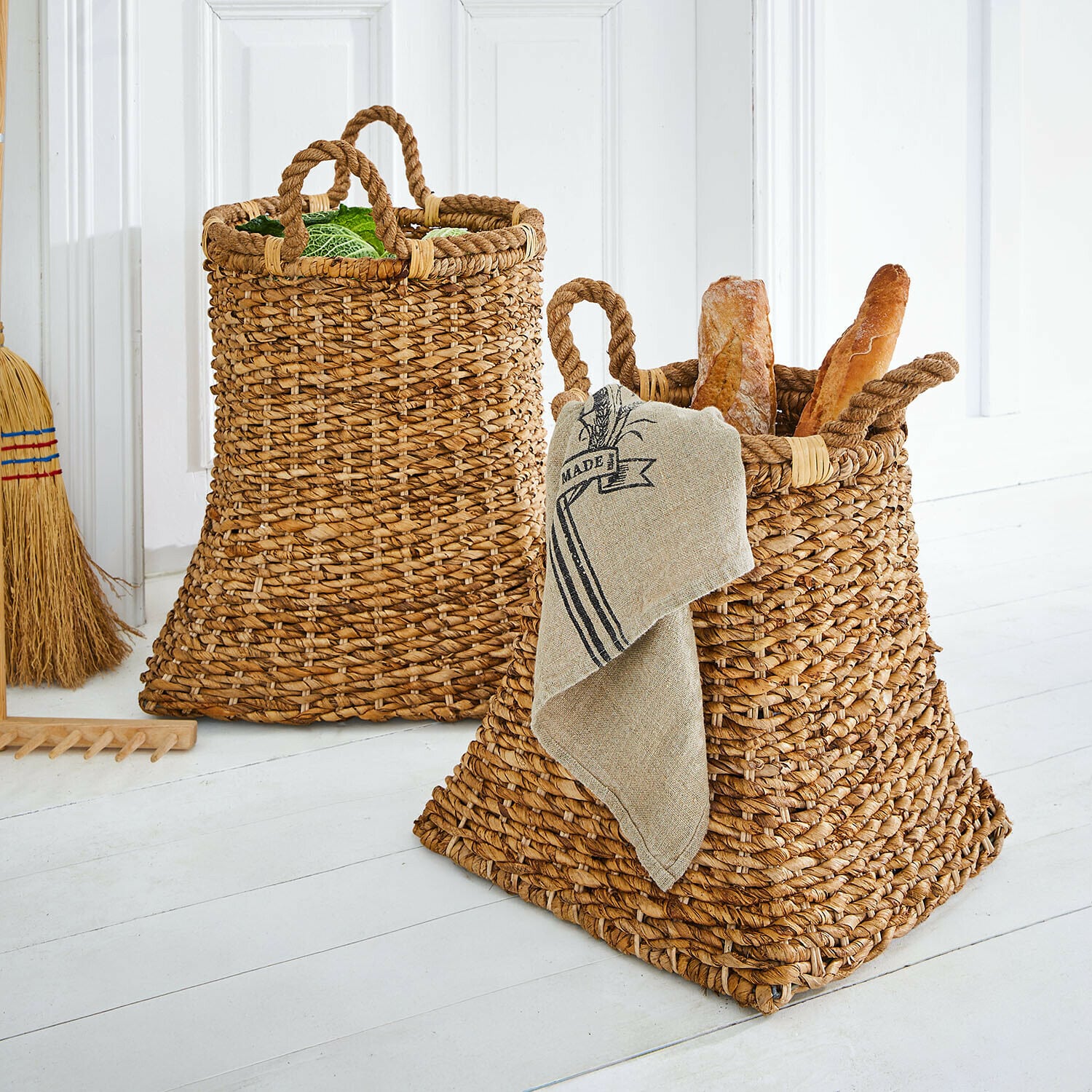 Coppia di cestini Saviani Due ceste intrecciate in colore naturale con manici, piene di pane e verdure in ambiente luminoso
