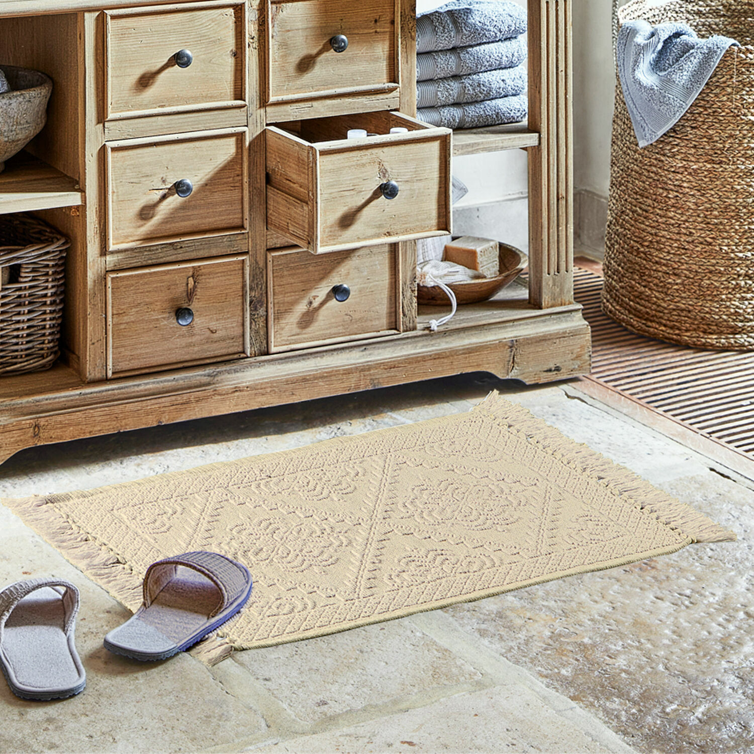 Tappeto beige in cotone con frange su pavimento in pietra davanti a mobile in legno in bagno