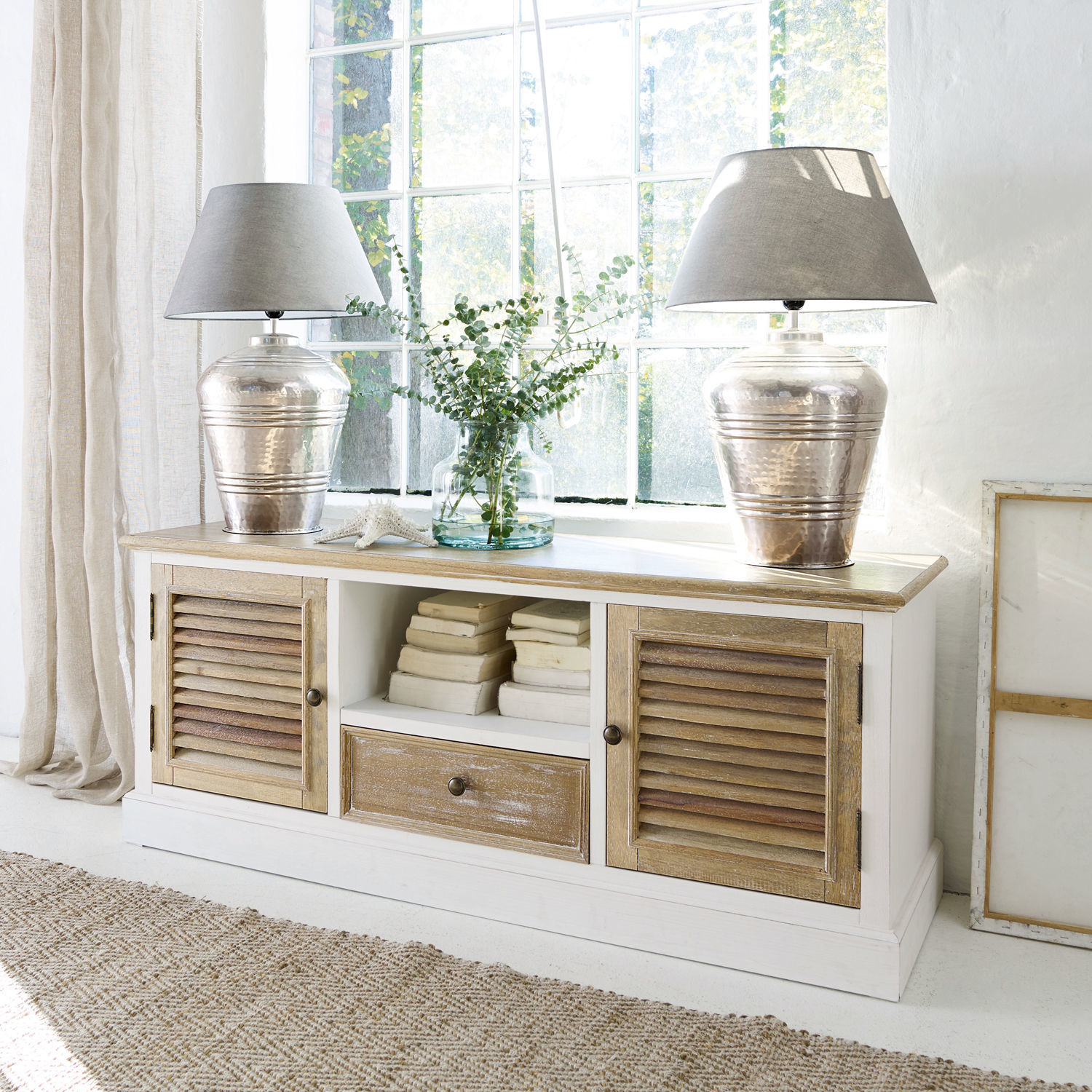 Credenza Glencoe Credenza in legno bianco con piano naturale e ante a persiana, decorata con lampade e libri