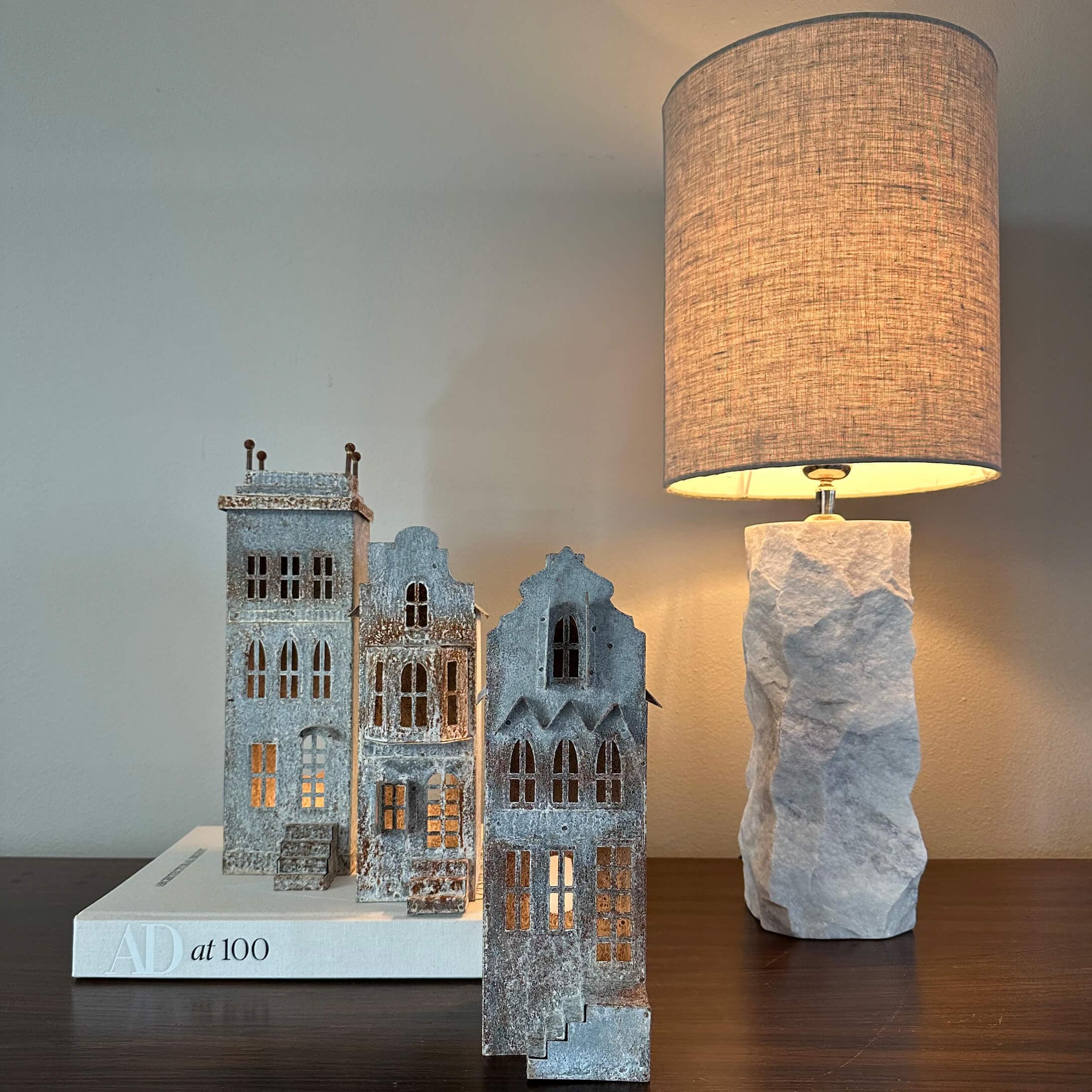 Case decorative in metallo grigio su libro bianco accanto a lampada con base in pietra