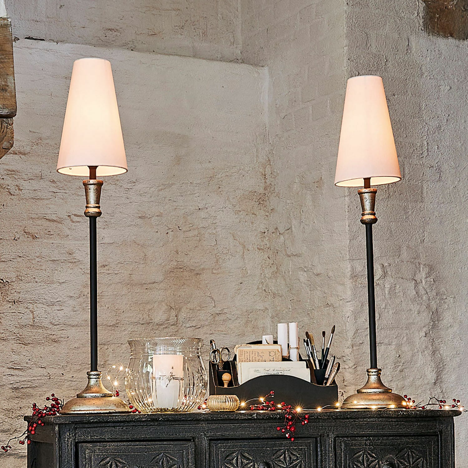 Coppia di lampade da tavolo Obsonville Coppia di lampade da tavolo con base in metallo e paralumi bianchi su una credenza scura decorata