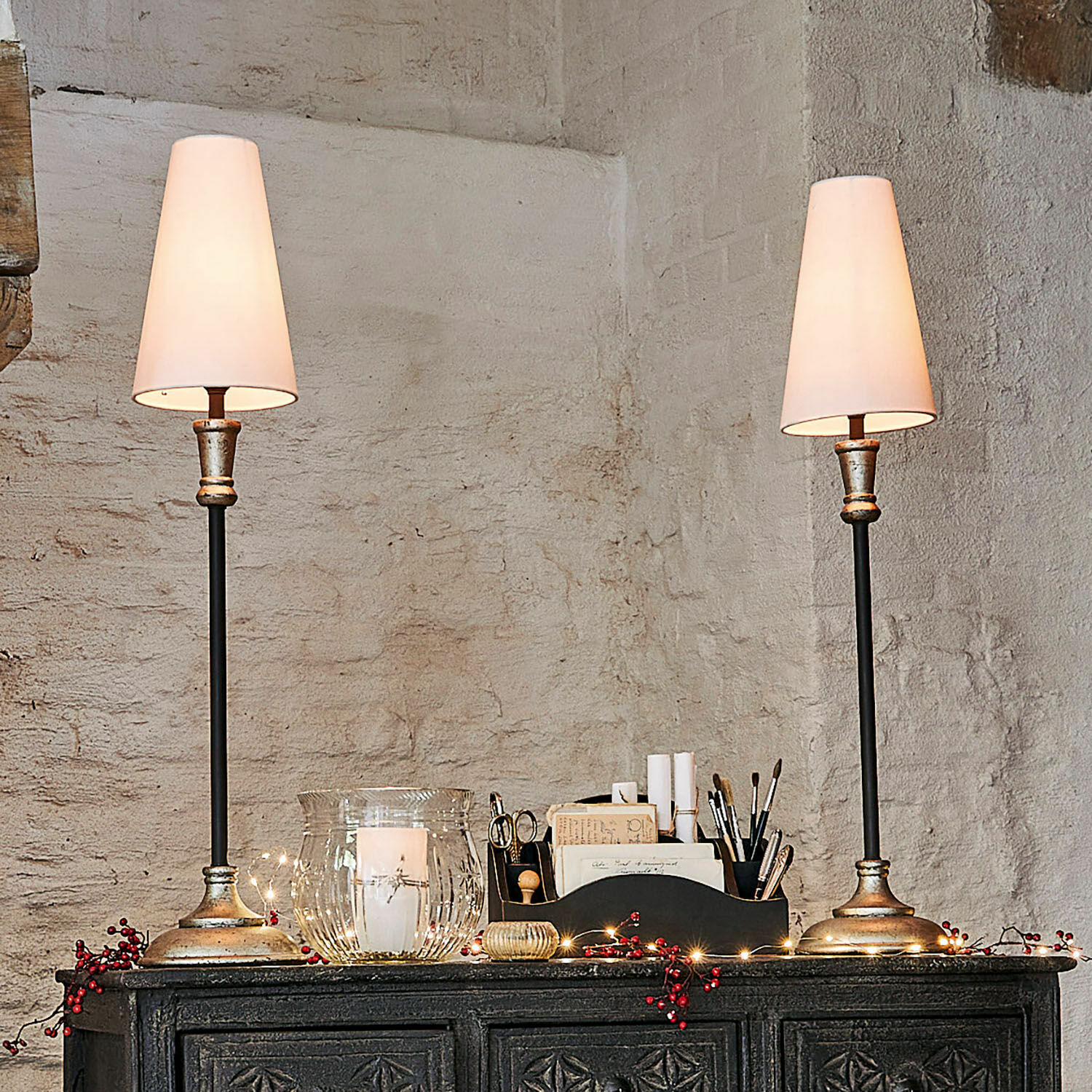 Coppia di lampade da tavolo Obsonville Coppia di lampade da tavolo con base in metallo e paralumi bianchi su una credenza scura decorata