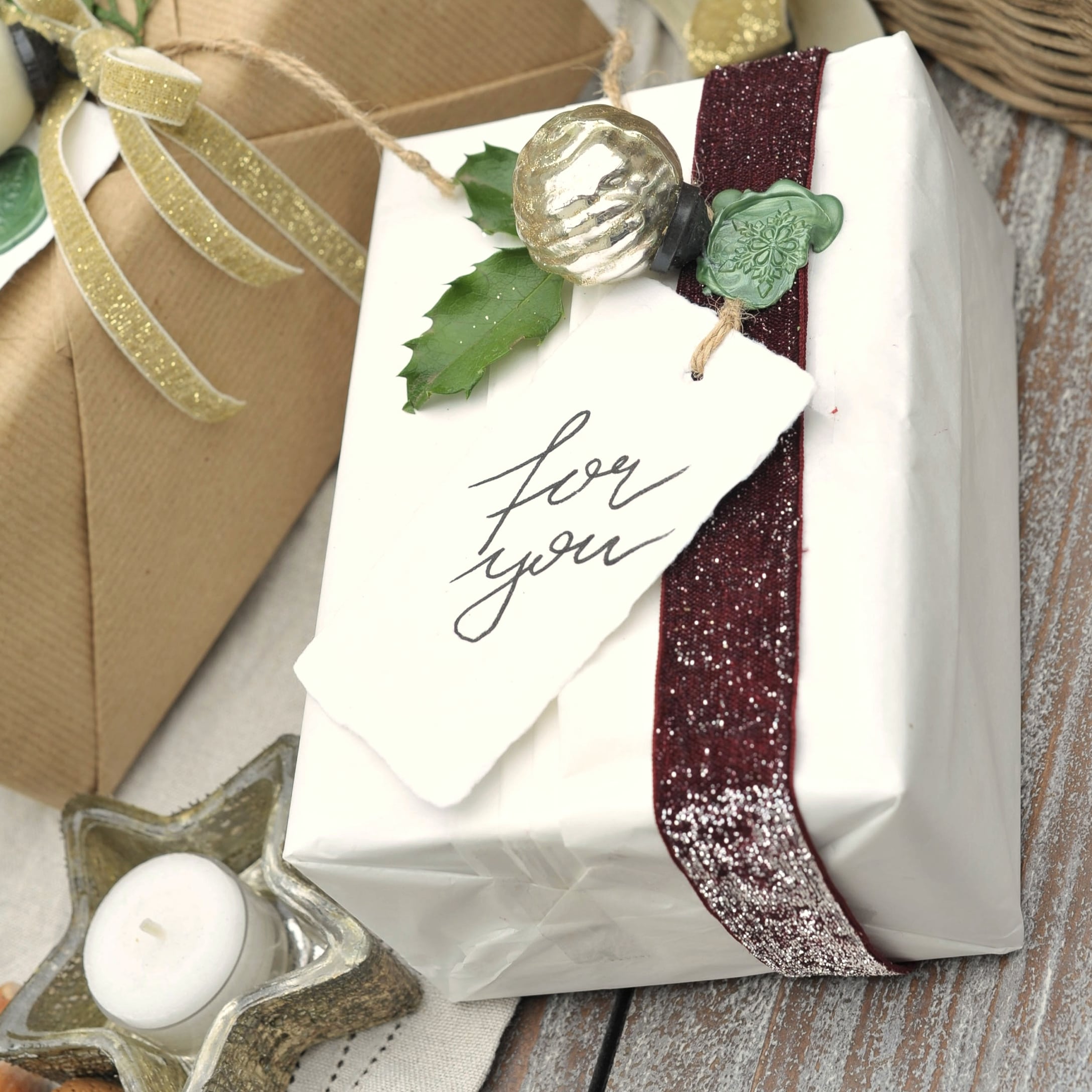 Regalo avvolto in carta bianca con nastro bordeaux e foglia verde, decorazione natalizia