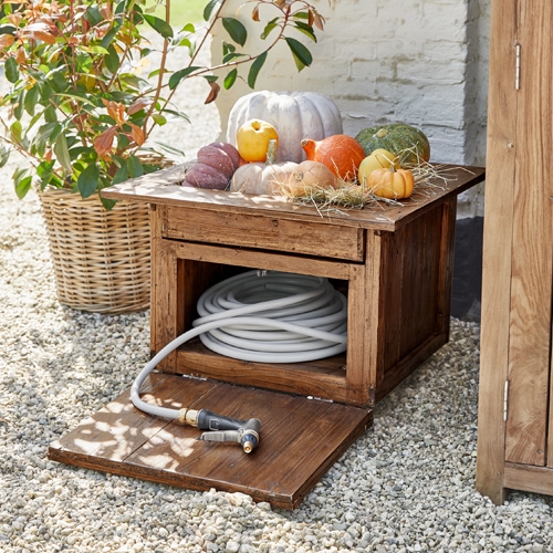 Cassa da giardino in legno con tubo bianco e zucche decorative su ghiaia
