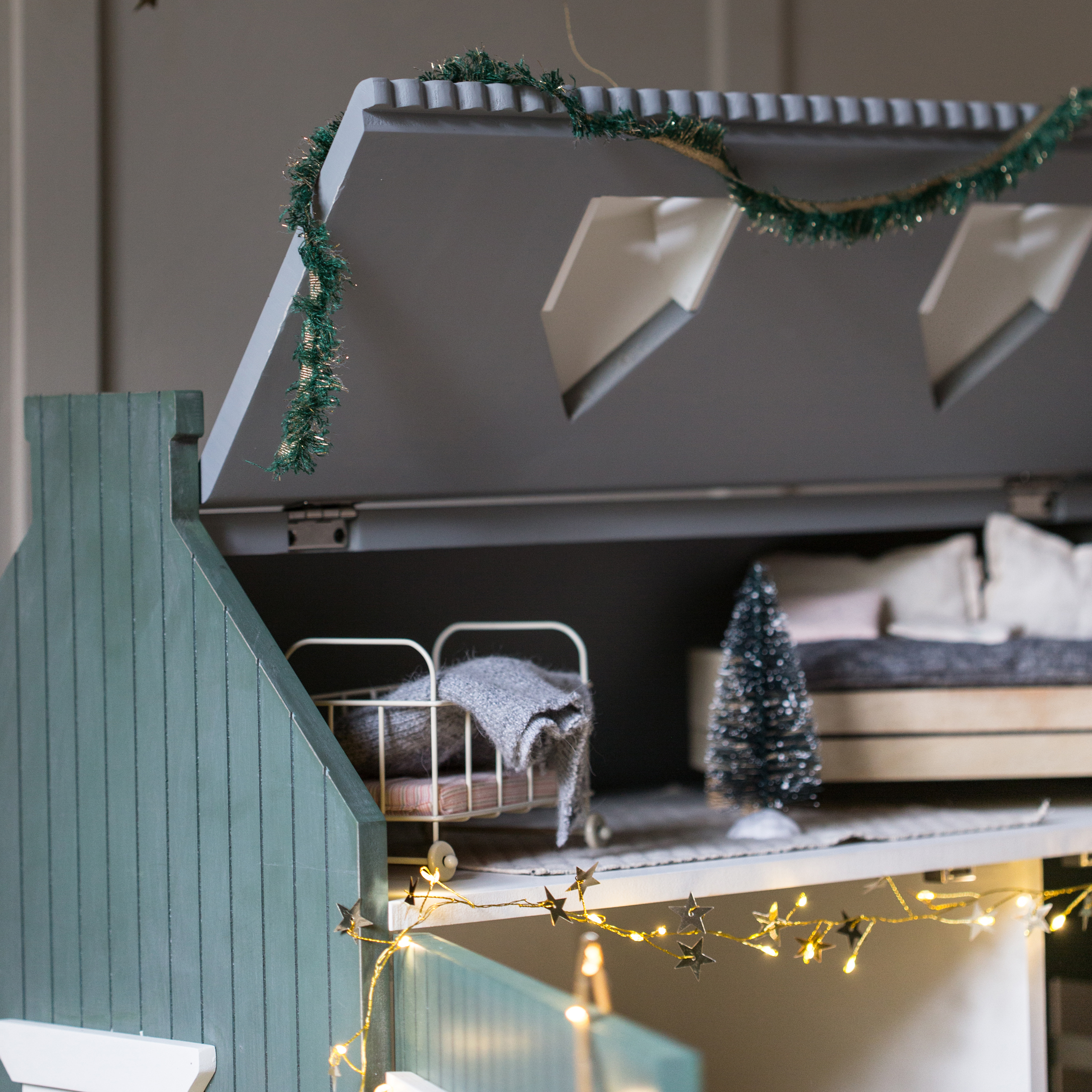 Casa delle bambole in legno con tetto verde, lettino e ghirlanda luminosa decorativa