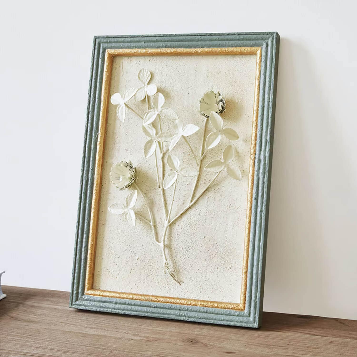 Rilievo decorativo floreale in cornice verde e oro con superficie strutturata su sfondo chiaro