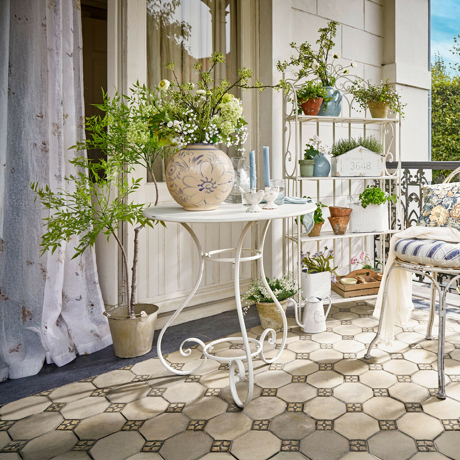 Tavolino Iteuil Tavolo in metallo bianco con vaso decorativo e fiori su terrazza con piante e sedia