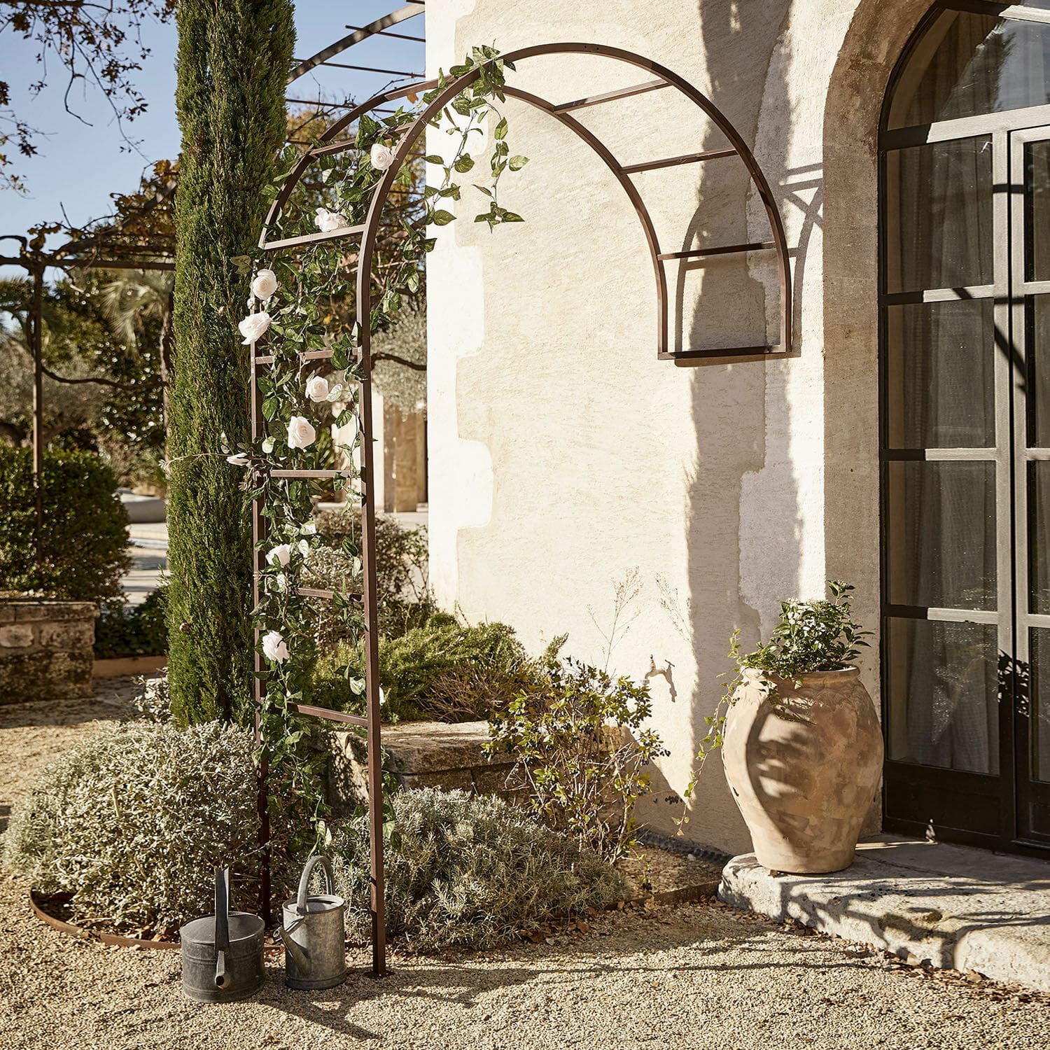 Arco da giardino Auburn Pergola da giardino in metallo marrone con arco decorato con rose bianche e annaffiatoi su ghiaia