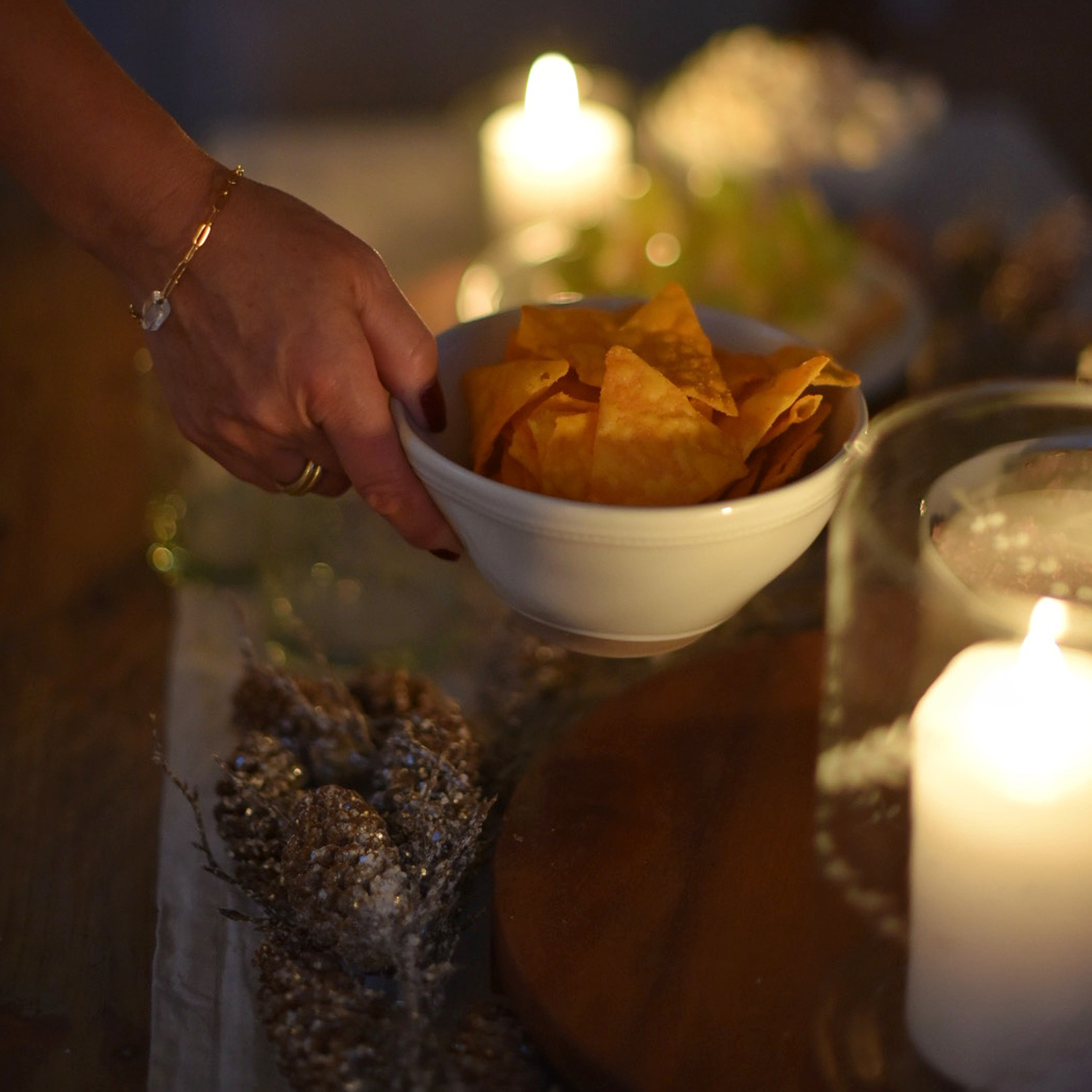 Mano che tiene una ciotola bianca con chips arancioni davanti a candele e decorazioni sfocate