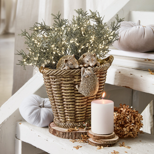 Cesto decorativo con tre ricci in resina e rami verdi con luci LED su tavolo bianco