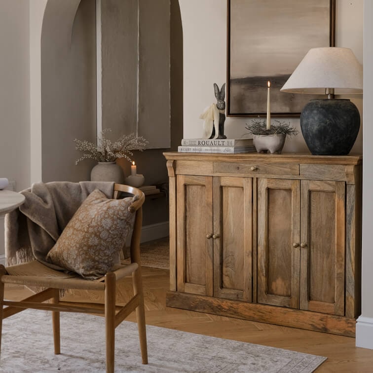Credenza in legno colore naturale con lampada e decorazioni in soggiorno accogliente con sedia e cuscino