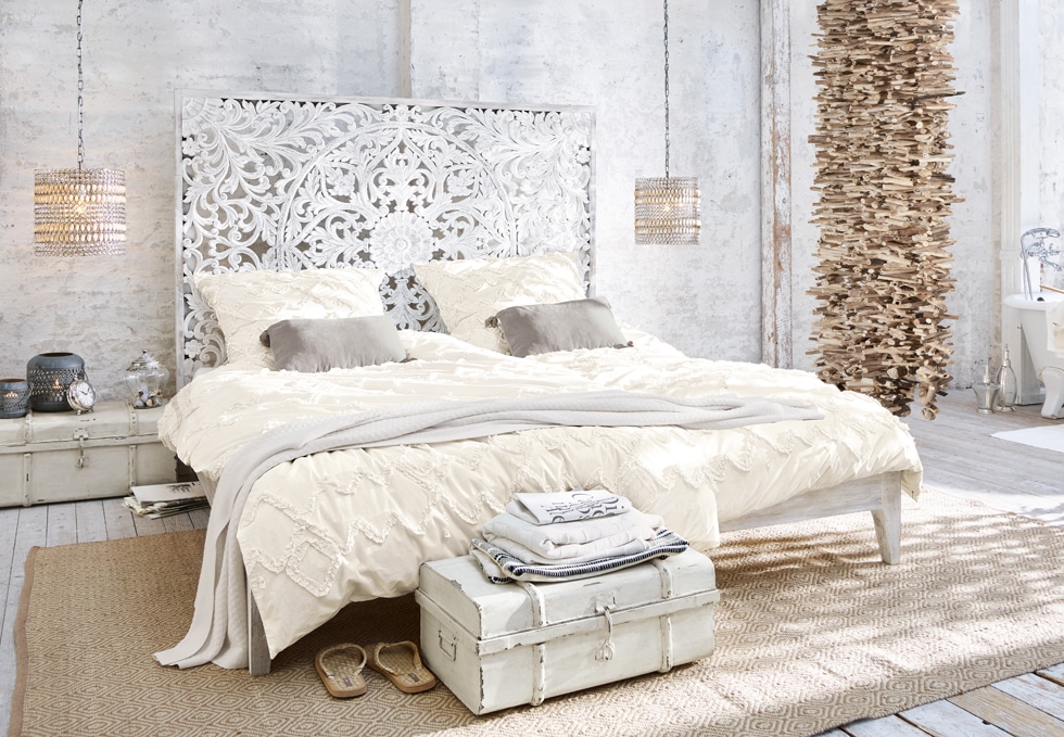 Camera da letto boho con letto bianco intagliato, biancheria crema e decorazioni naturali in legno