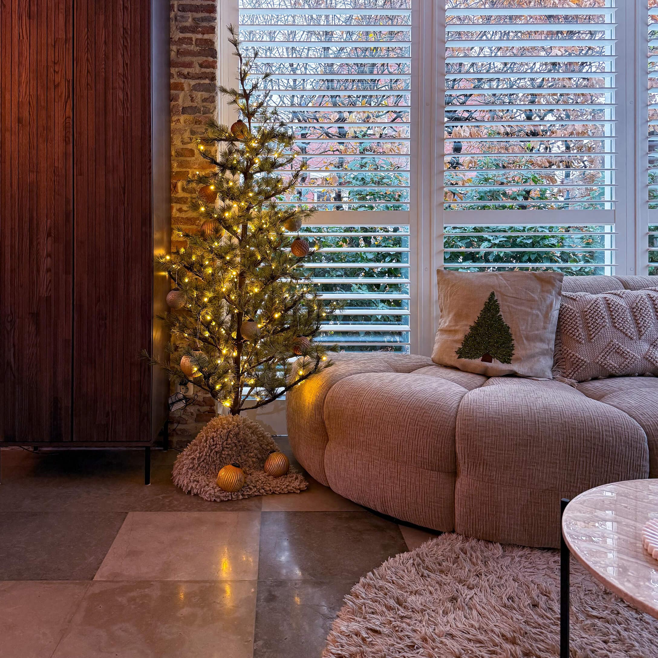 Soggiorno accogliente con divano beige, cuscino con albero di Natale e piccolo albero decorativo illuminato a LED