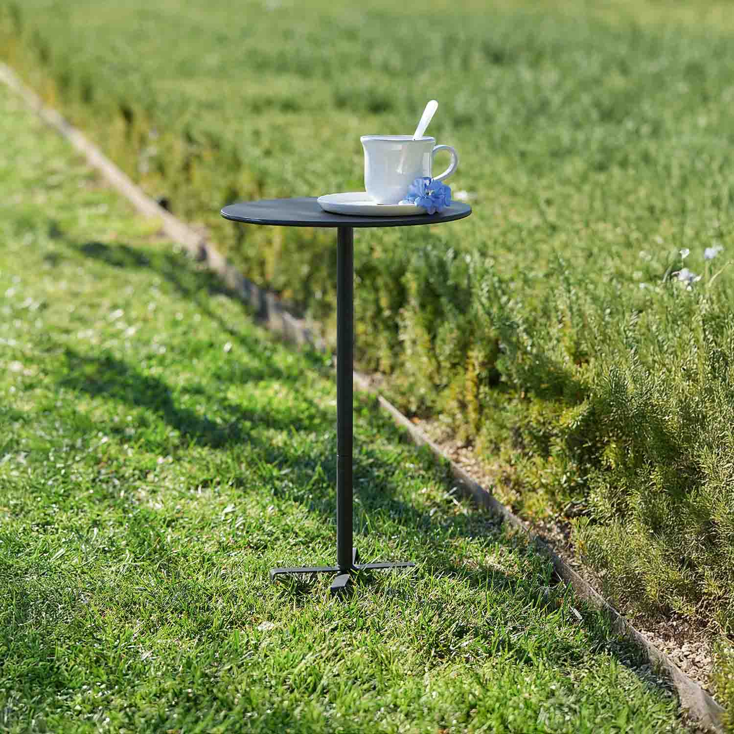 Piccolo tavolo da giardino nero in metallo con tazza bianca e fiore blu sull'erba