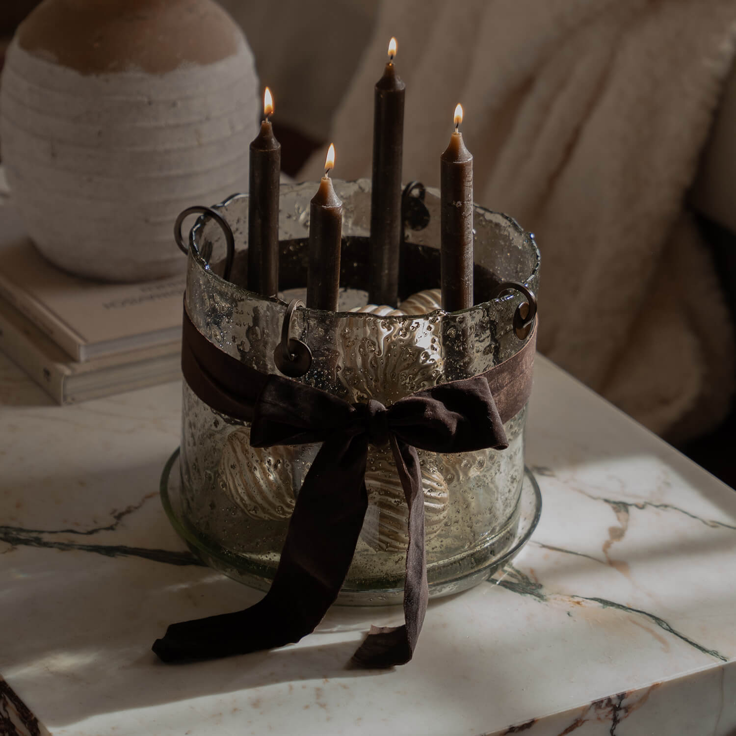 Portacandele in vetro con quattro candele marroni e fiocco decorativo su tavolo in marmo