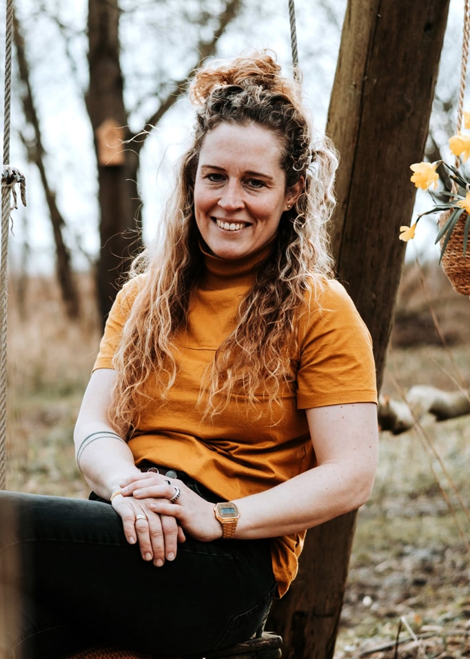 Donna con dolcevita arancione seduta su un'altalena in un bosco autunnale, luce naturale